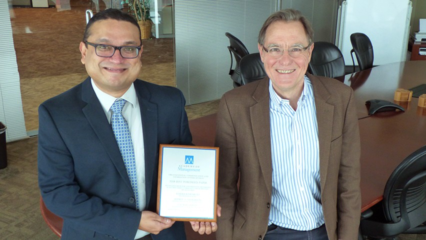 Two faculty holding their award from the Academy of Management in a conference room at Stevens. 