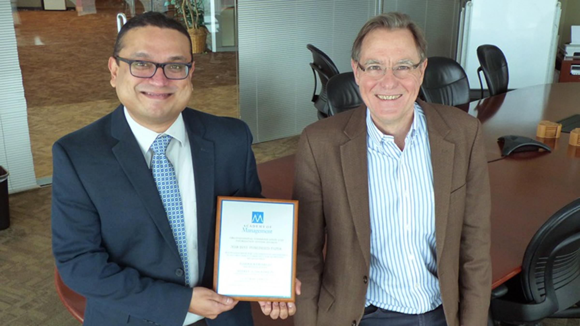 Two faculty holding their award from the Academy of Management in a conference room at Stevens.