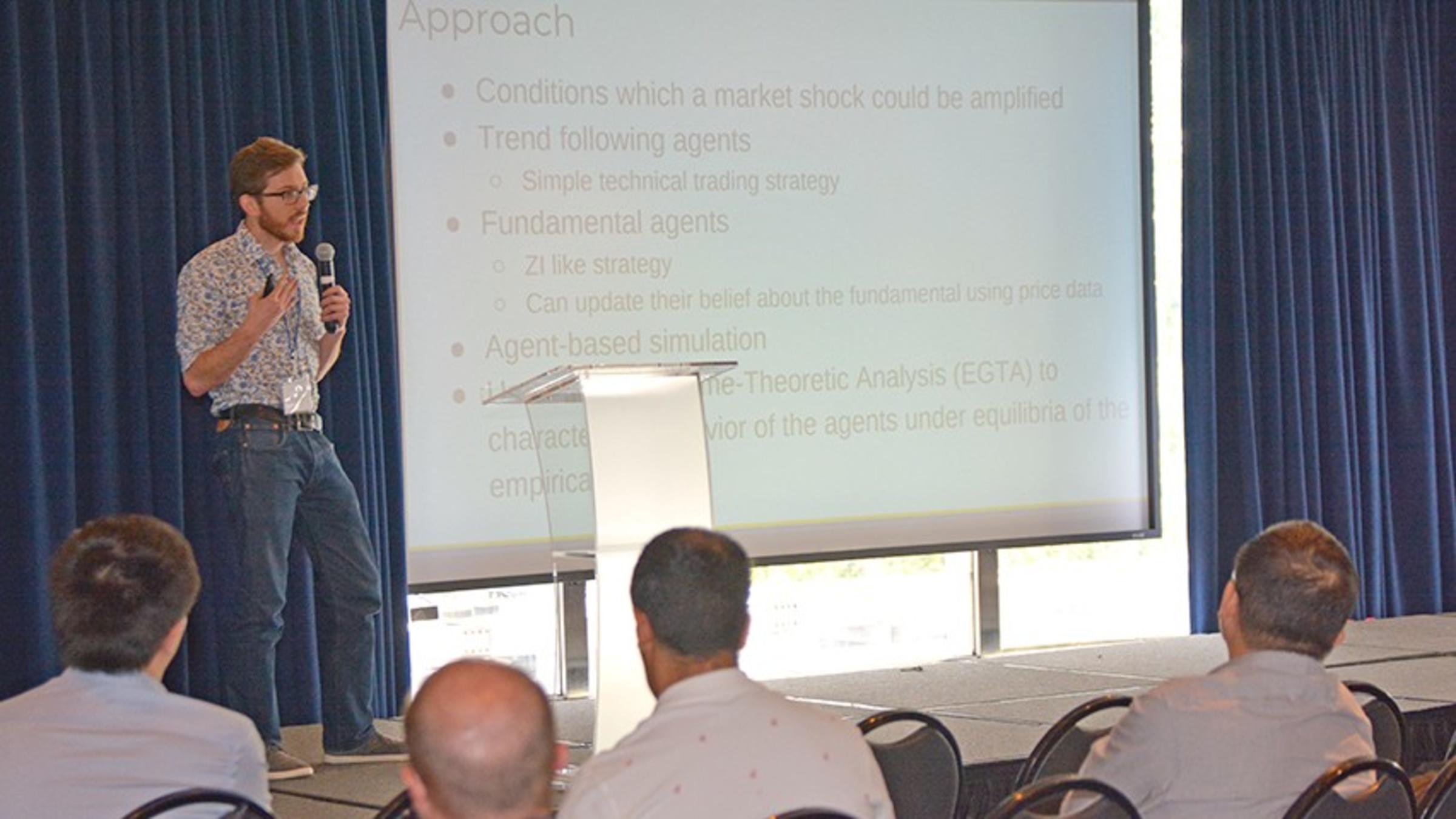 A male presenter delivers a talk at a podium in a conference space at the Stevens campus.