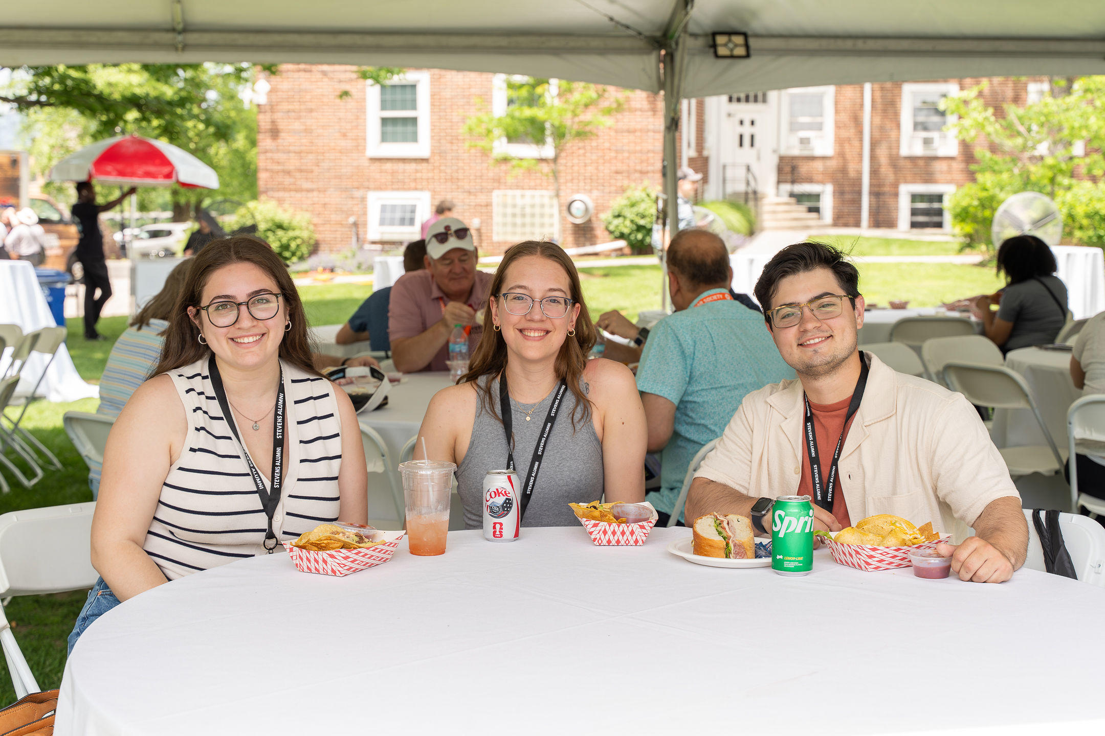 Three young alumni seated at a table outdoors during Stevens Alumni Weekend 2026