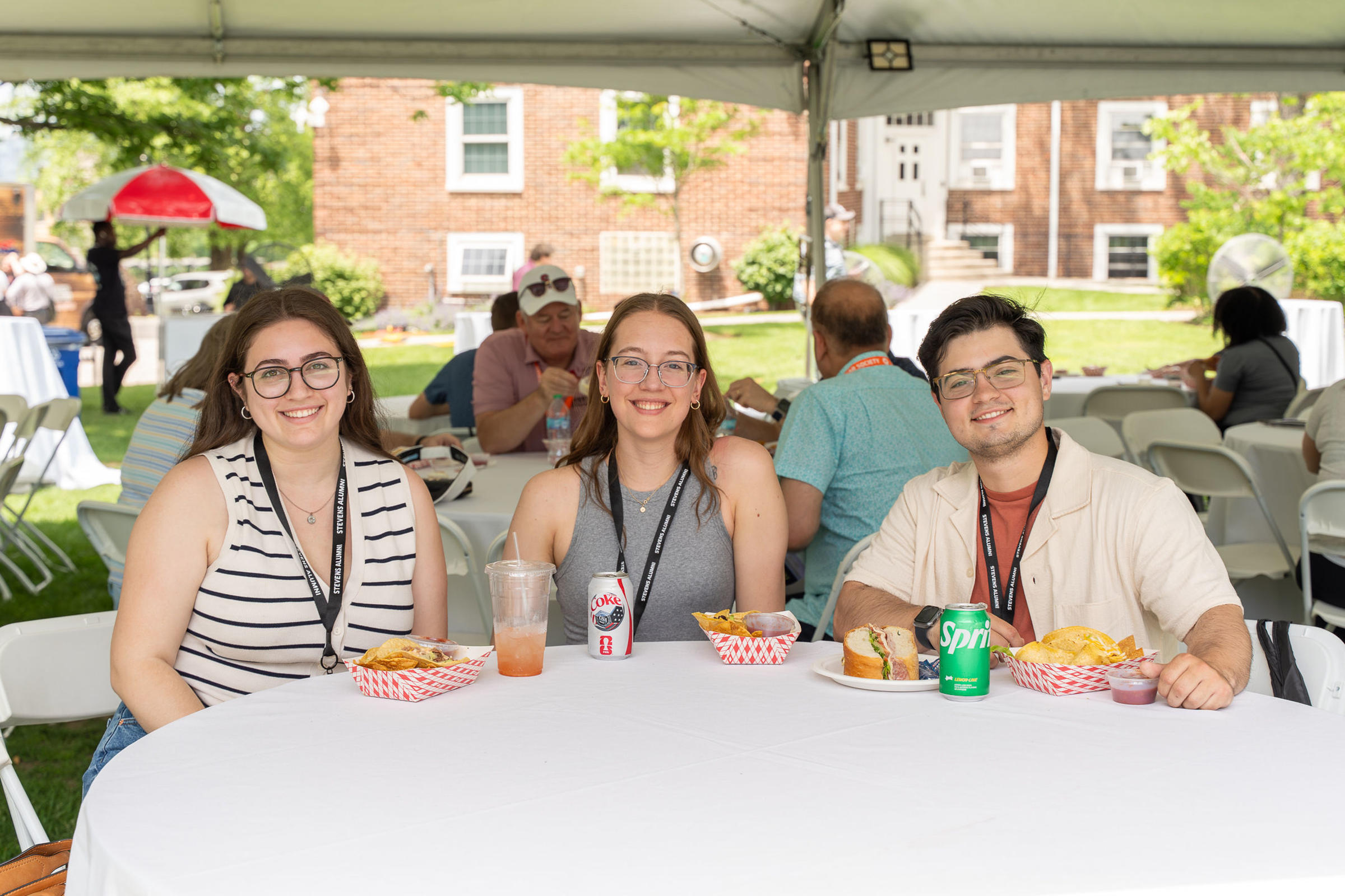 Three young alumni seated at a table outdoors during Stevens Alumni Weekend 2026