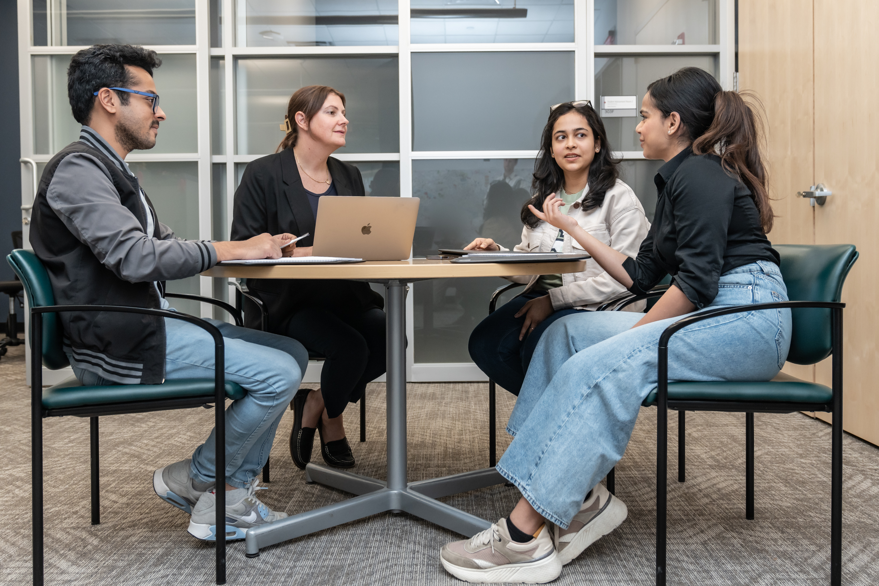 Small group of four individuals gather around a table talking to one another