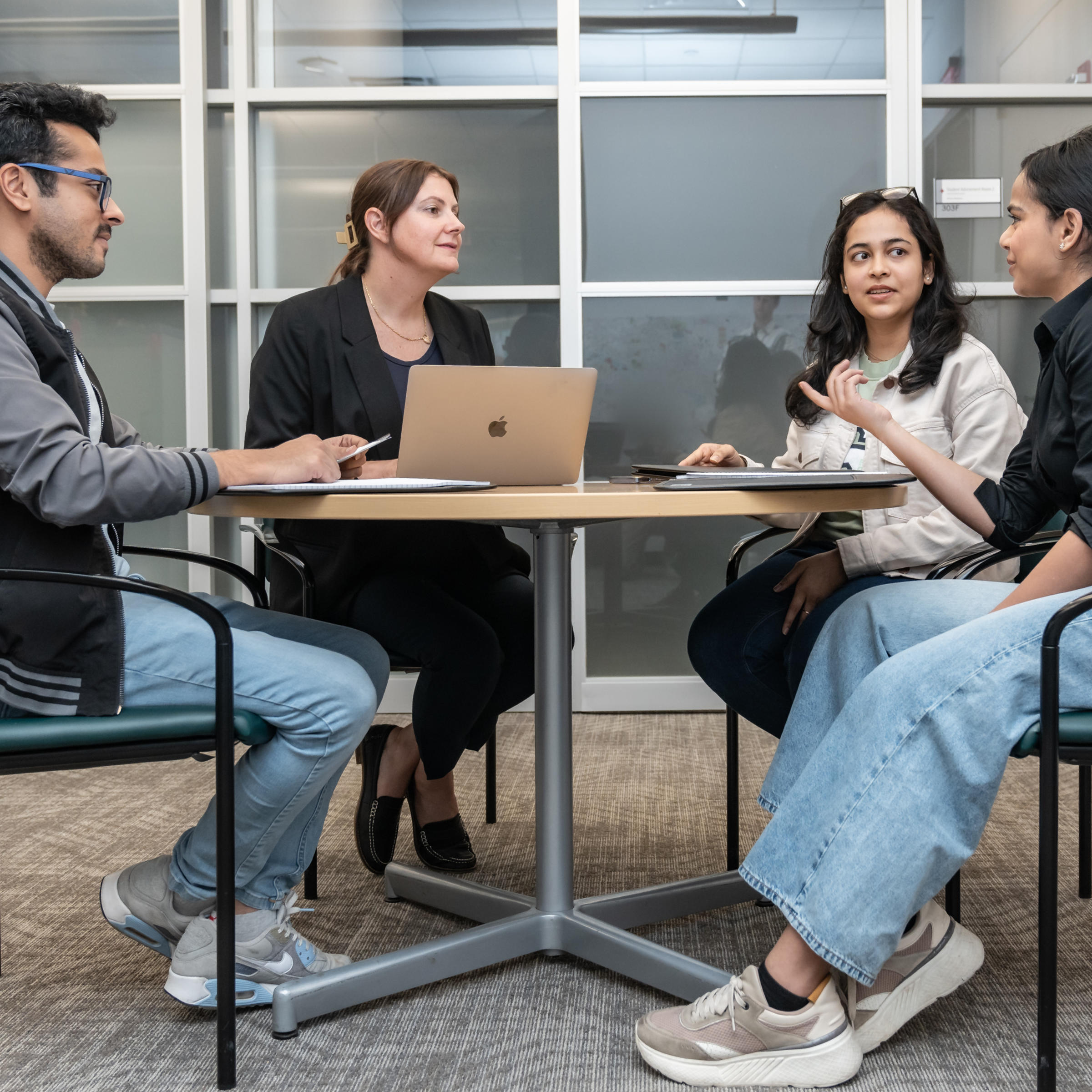 Small group of four individuals gather around a table talking to one another