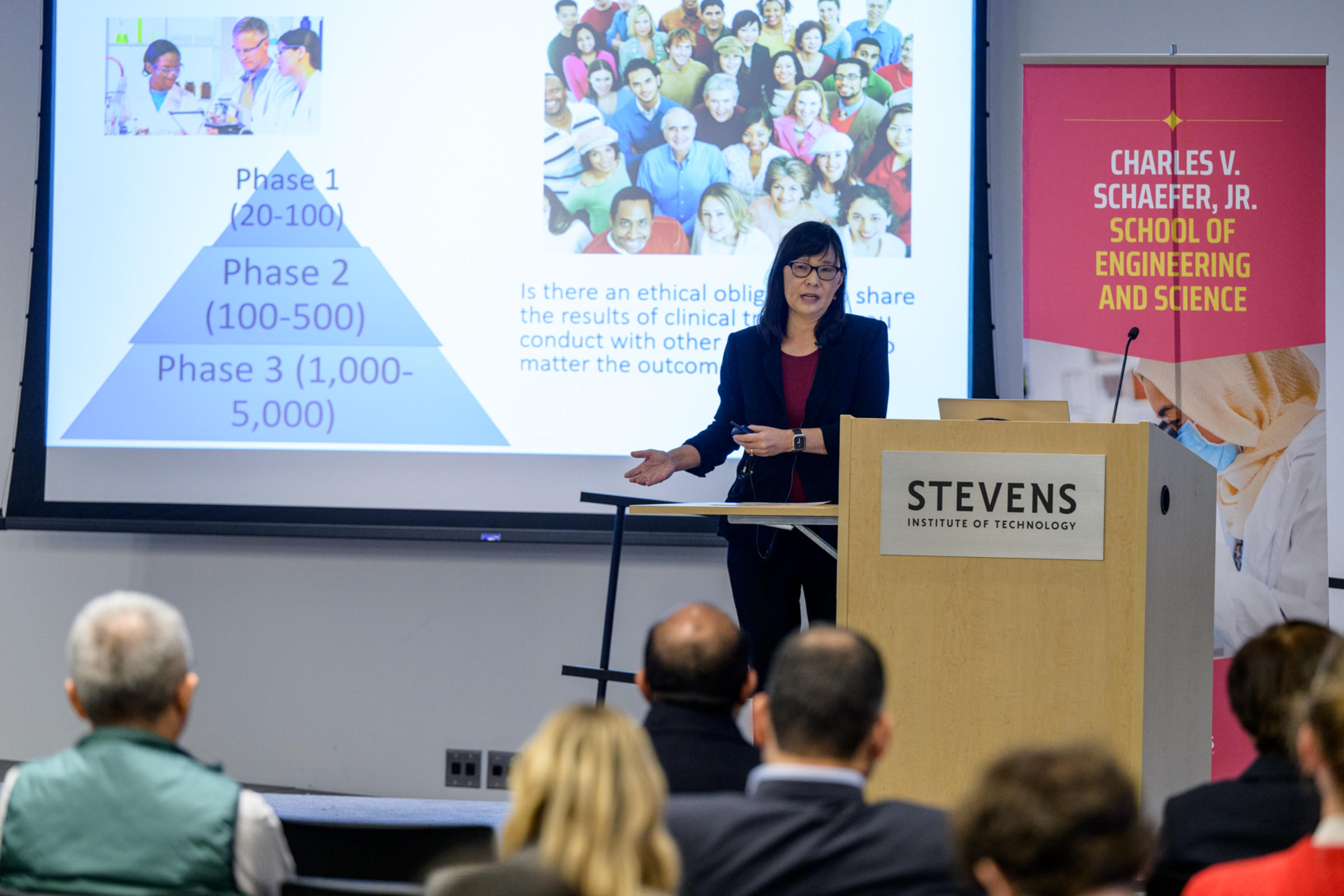 Rebecca Li speaks behind a podium with a slide showing a graphic reading Phase 1, Phase 2 and Phase 2 in the background.