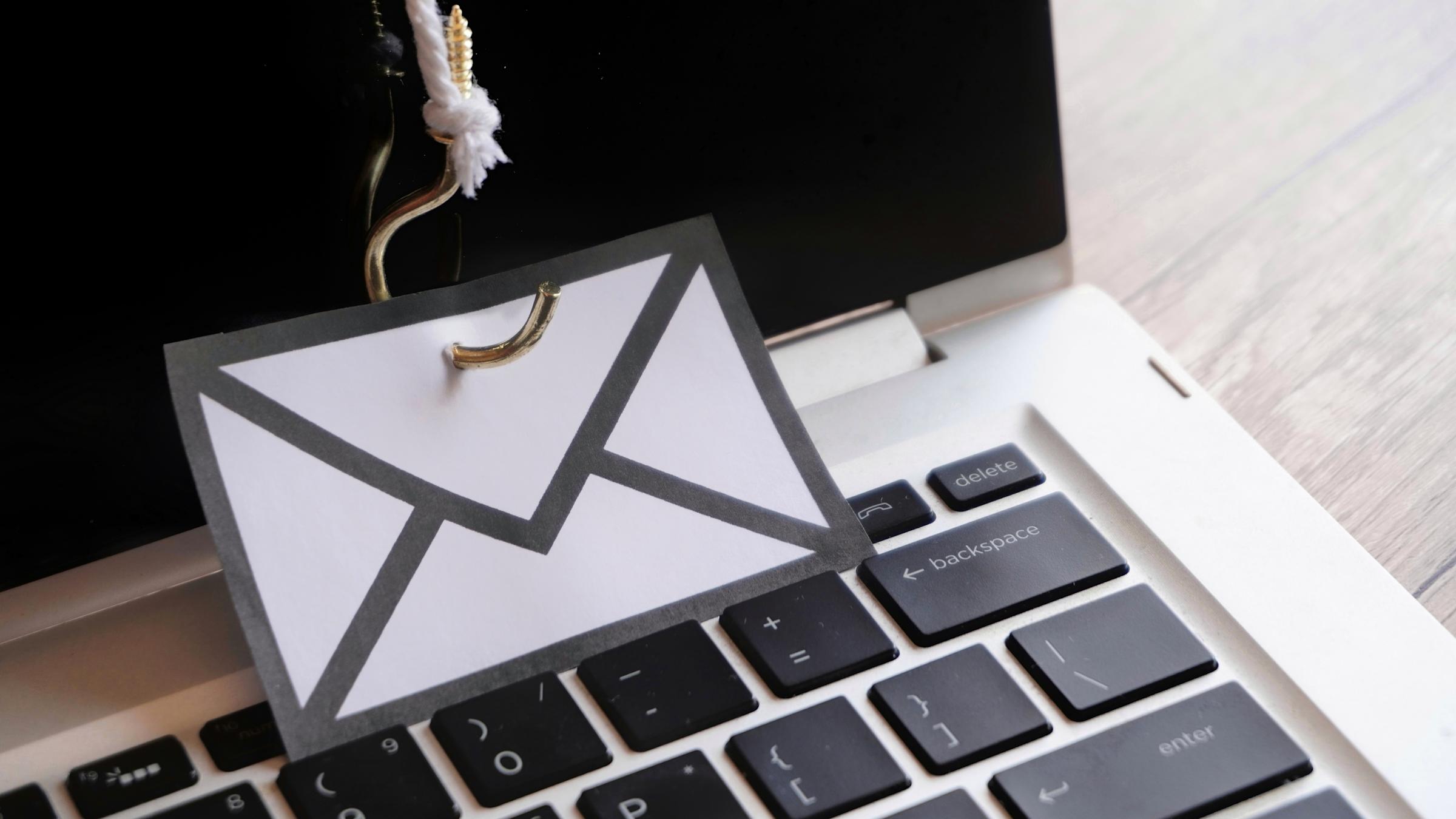 Closeup image of mail with hook on top of keyboard. Phishing email, malware and cyber security concept