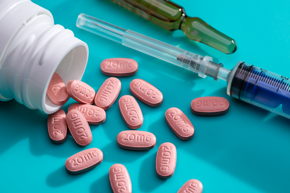 Photo of an open prescription bottle with pills falling out labeled "20MG," as well as a needle and syringe