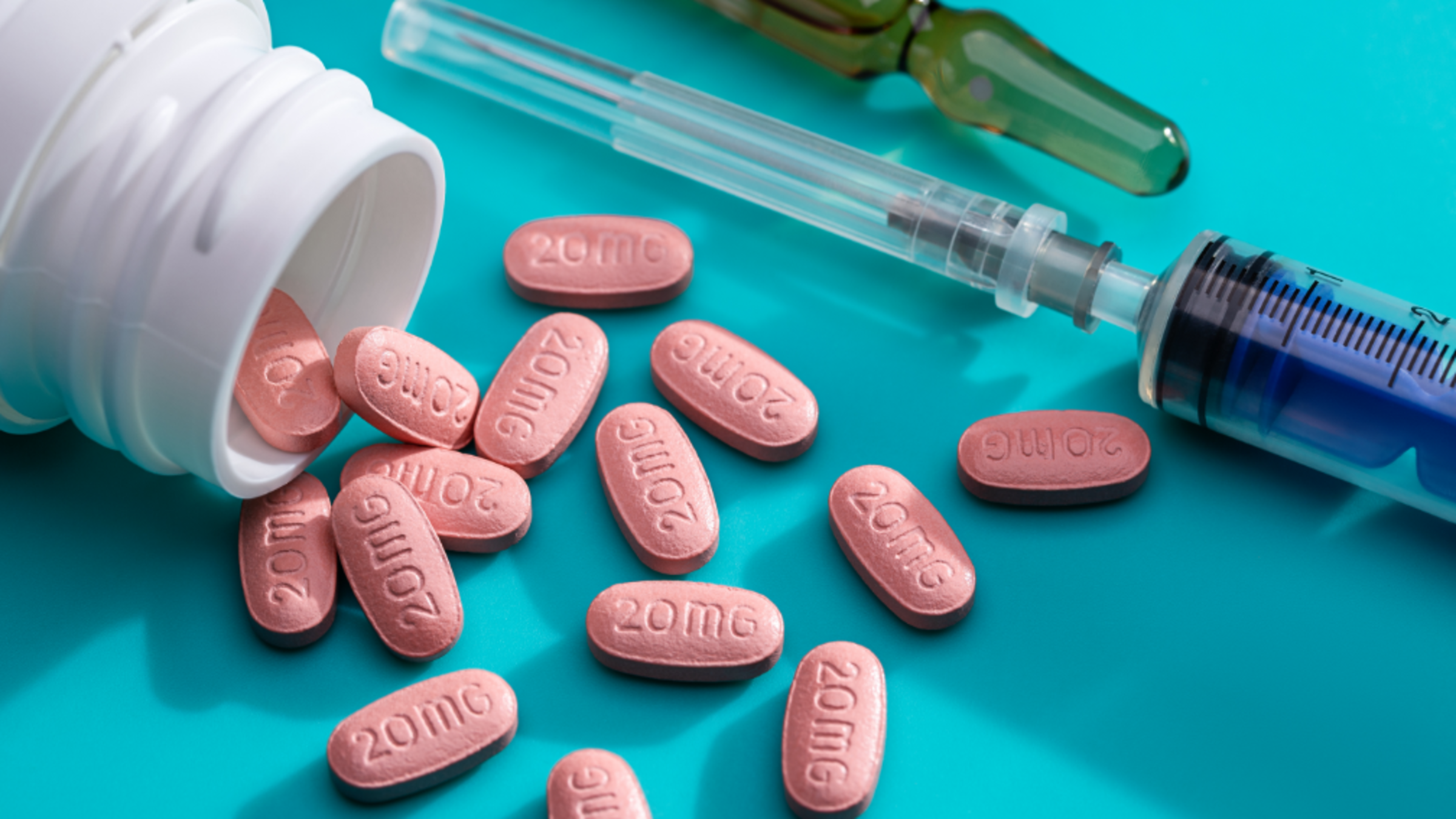 Photo of an open prescription bottle with pills falling out labeled "20MG," as well as a needle and syringe