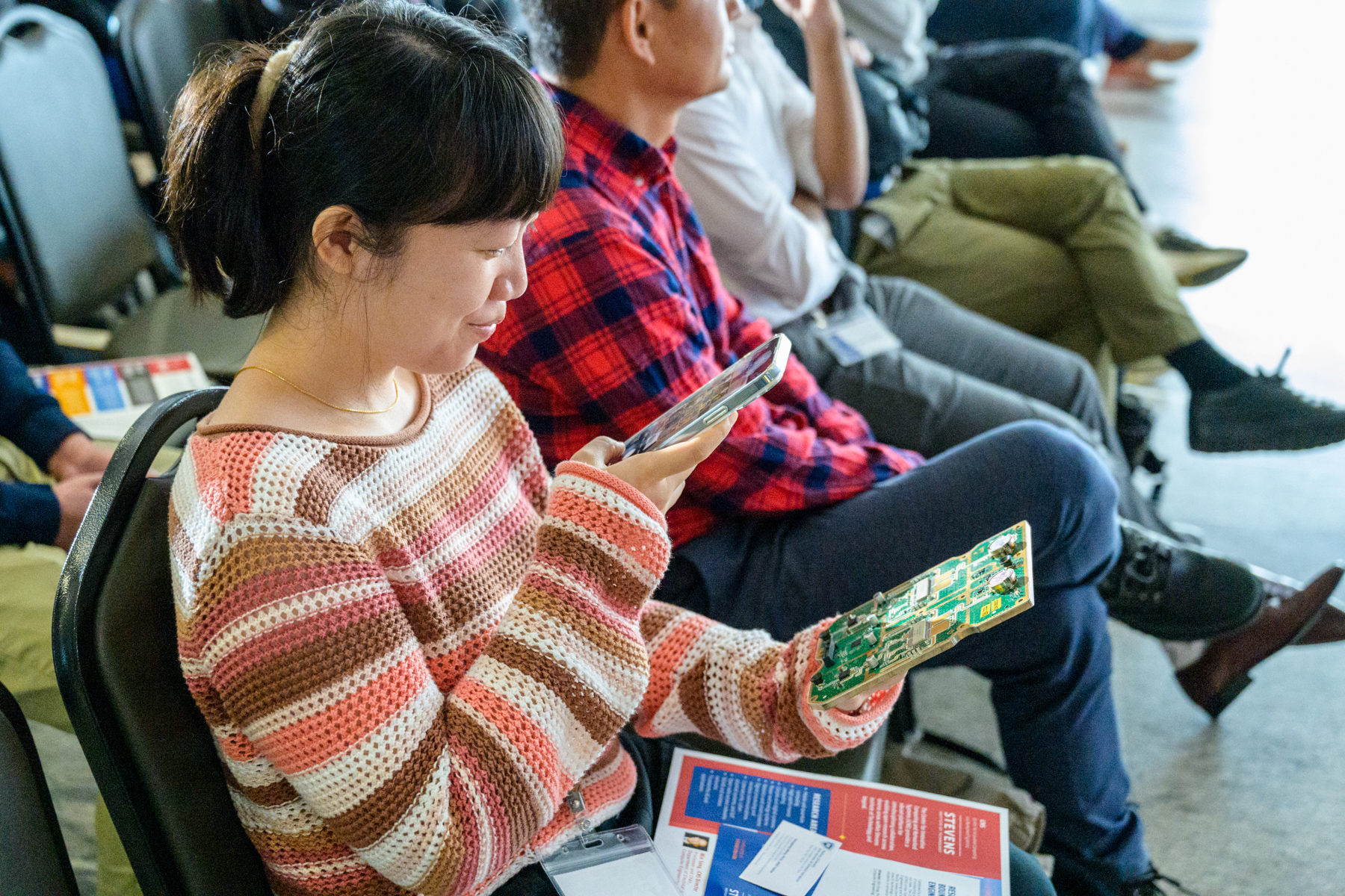 A student examines an electrical board with her phone.