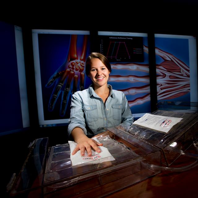 A photo of a female student sitting at a table with images of the physiology of a hand in the background
