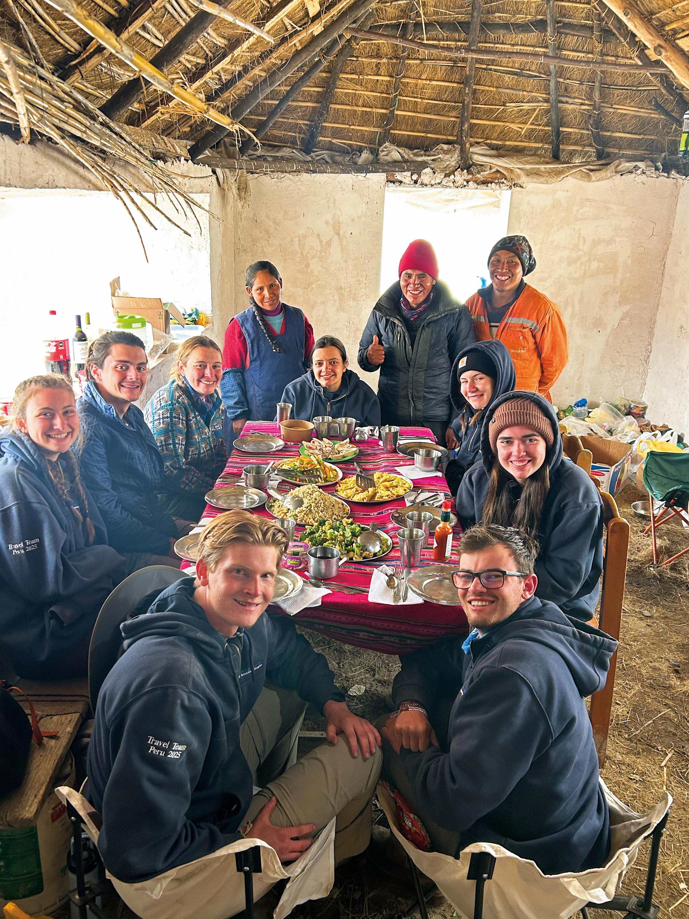 Students and community members gather around a table for a meal.