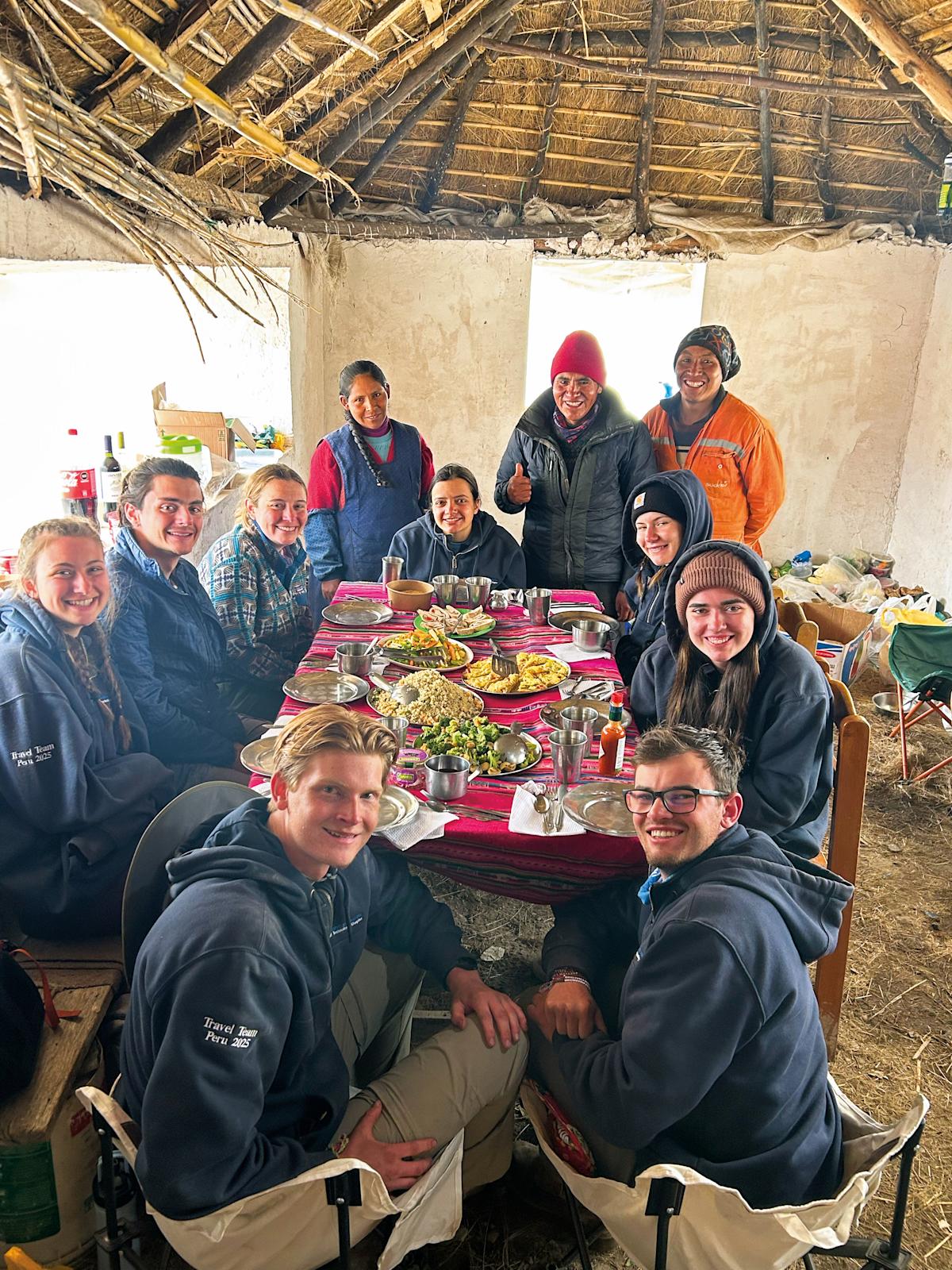Students and community members gather around a table for a meal.