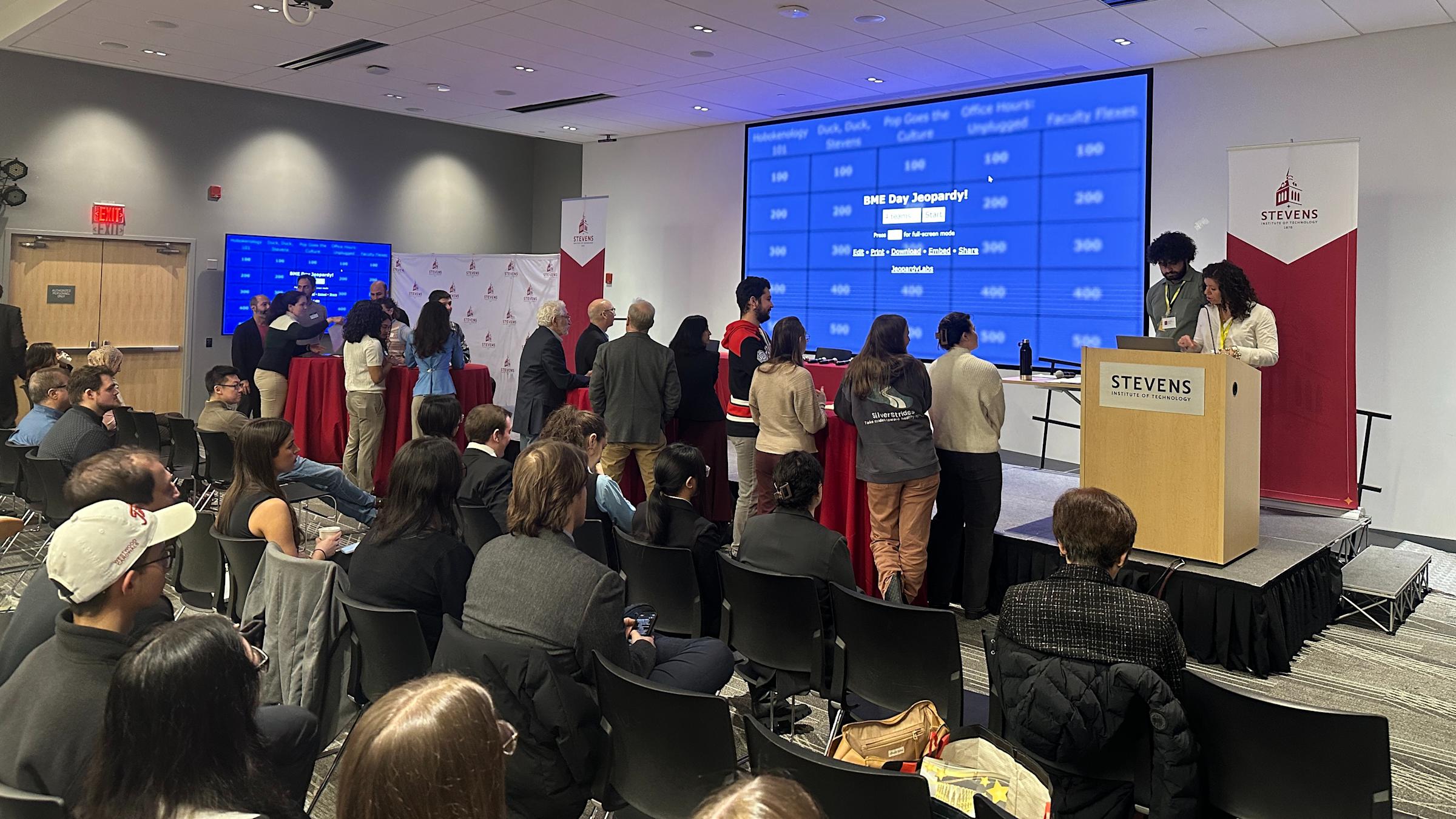Groups of students and faculty gather at the front of the conference room to participate in a Biomedical Engineering Day themed game of Jeopardy.