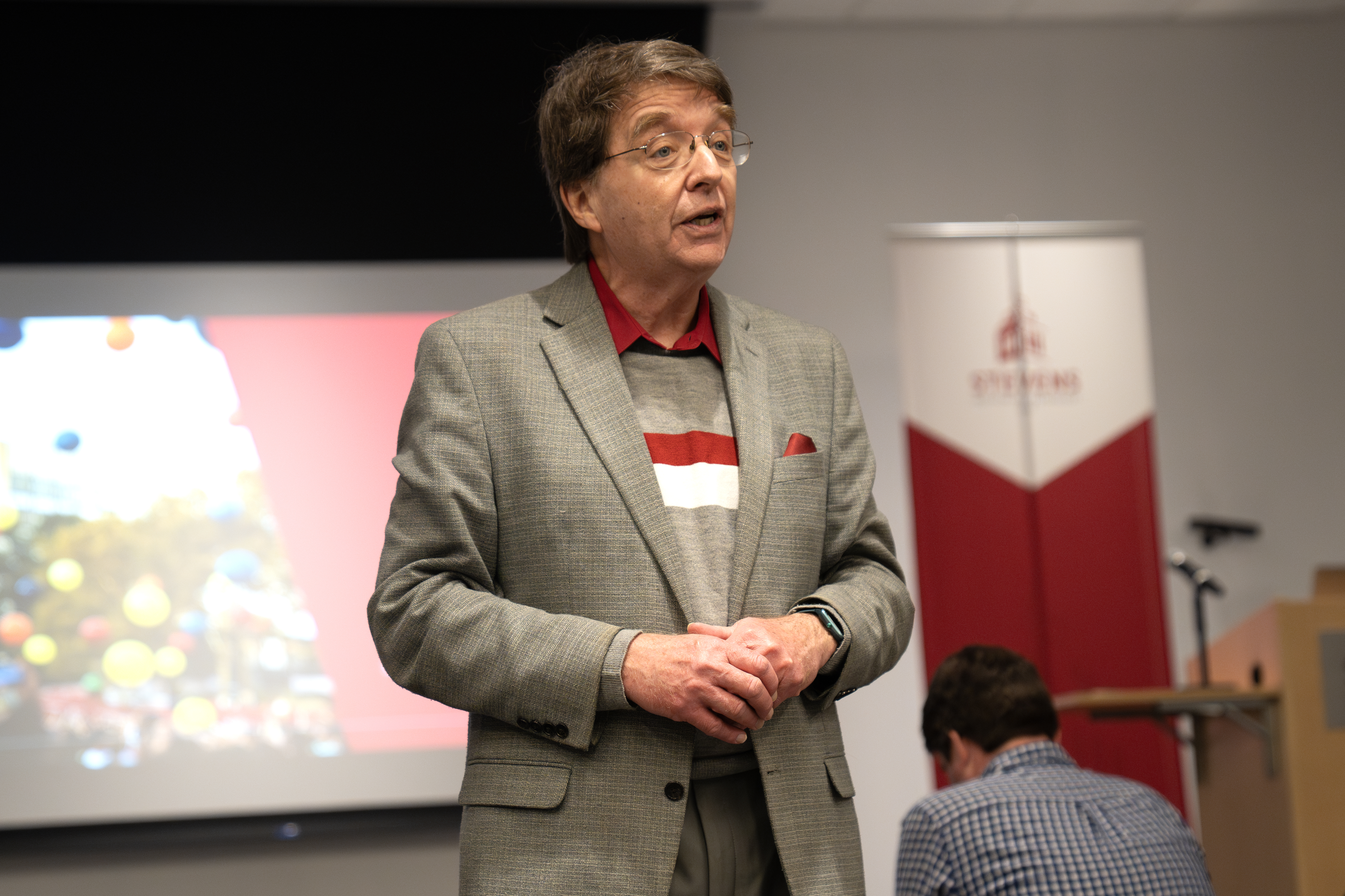 Professor Kevin Ryan stands with his hand clasped talking to the audience.
