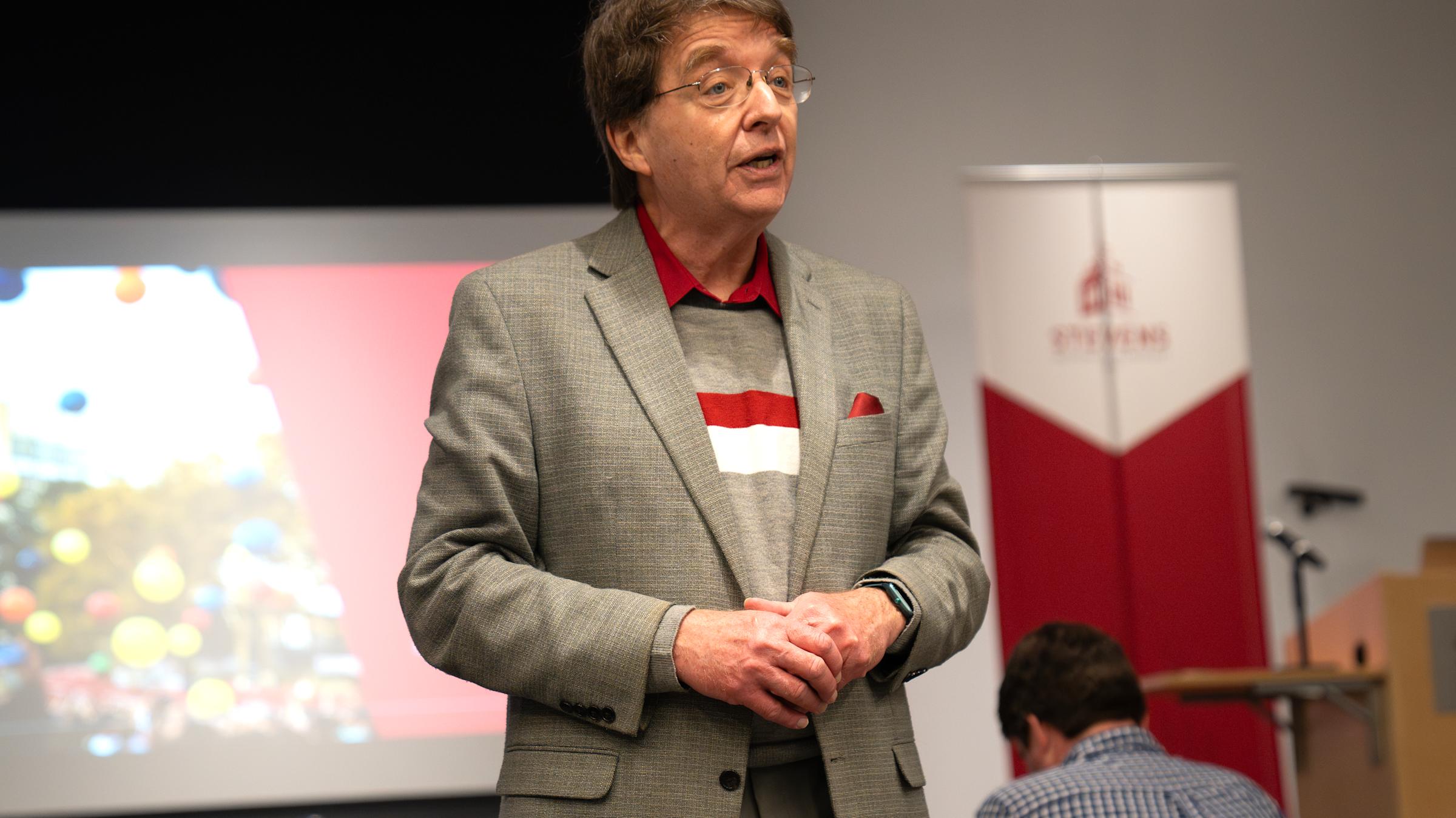 Professor Kevin Ryan stands with his hand clasped talking to the audience.