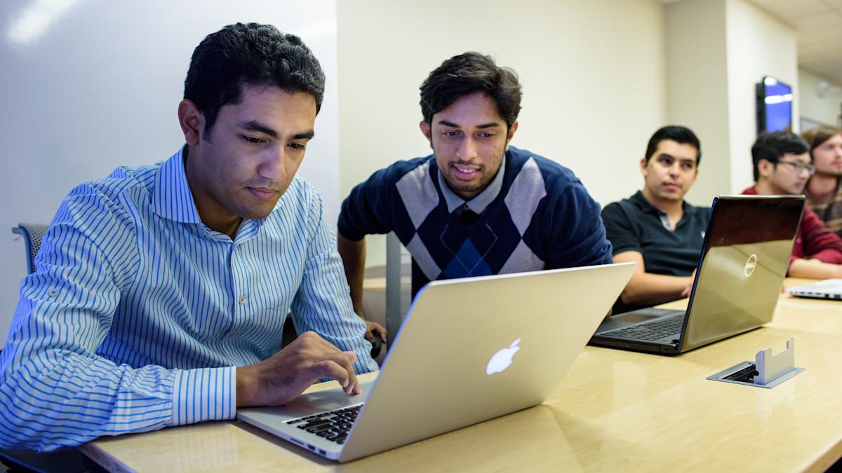 Two students smiling while looking at shared laptop.