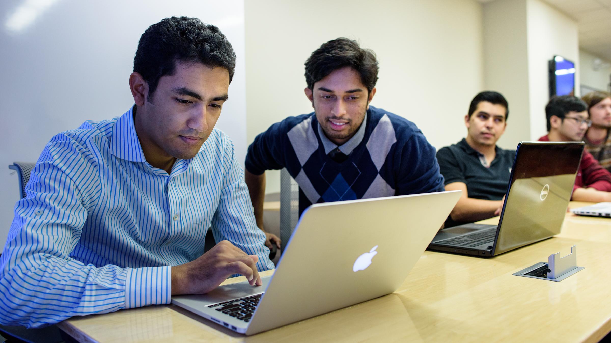 Two students smiling while looking at shared laptop.