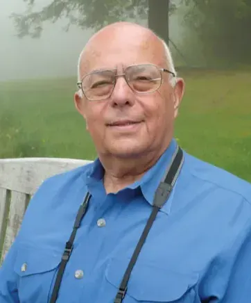 Edward Friedman Professor Emeritus sitting on a bench in a park wearing a blue shirt.