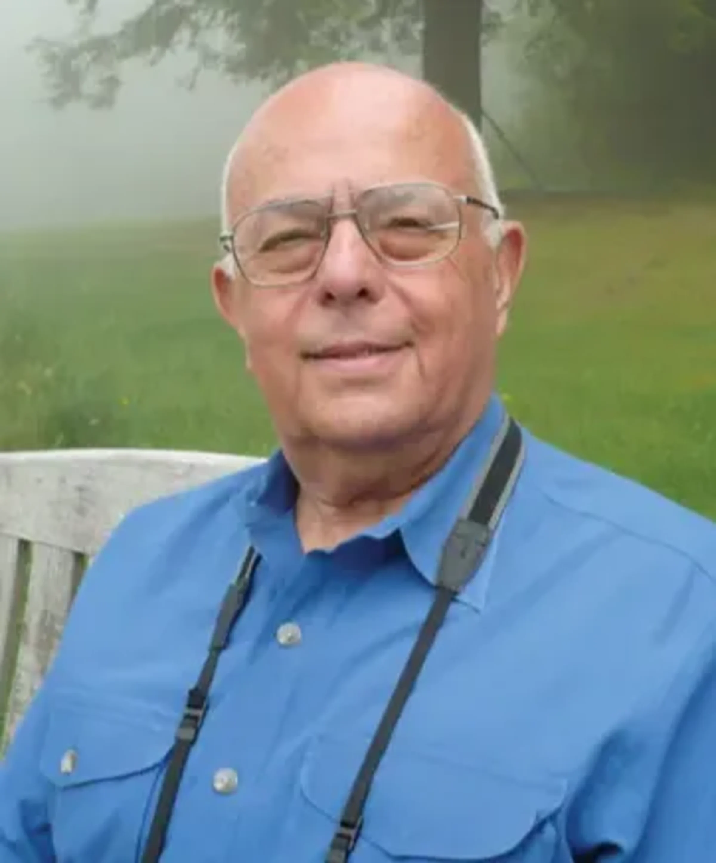 Edward Friedman Professor Emeritus sitting on a bench in a park wearing a blue shirt.