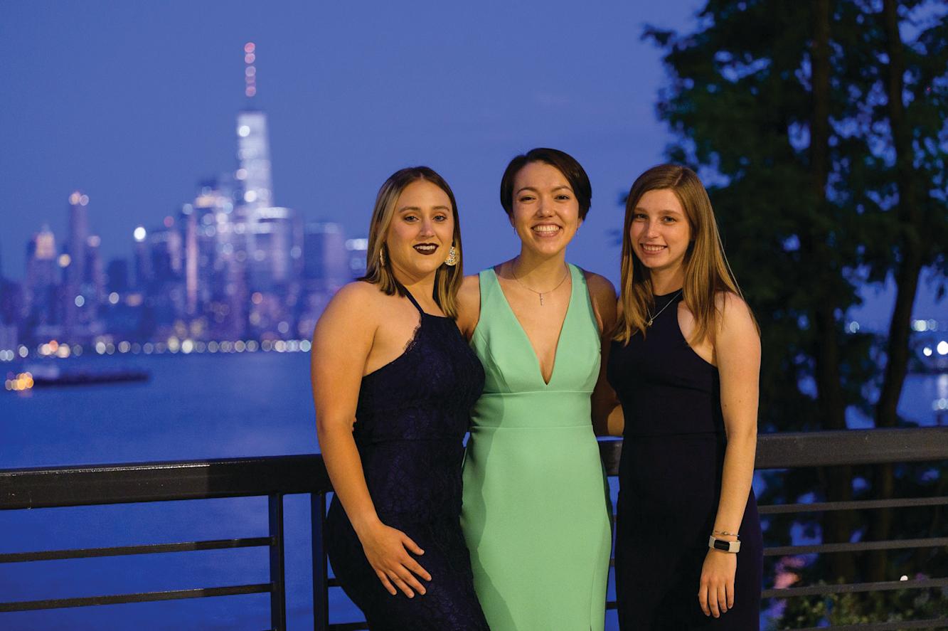 Three alumni smile for the camera in the evening with the New York skyline behind them.