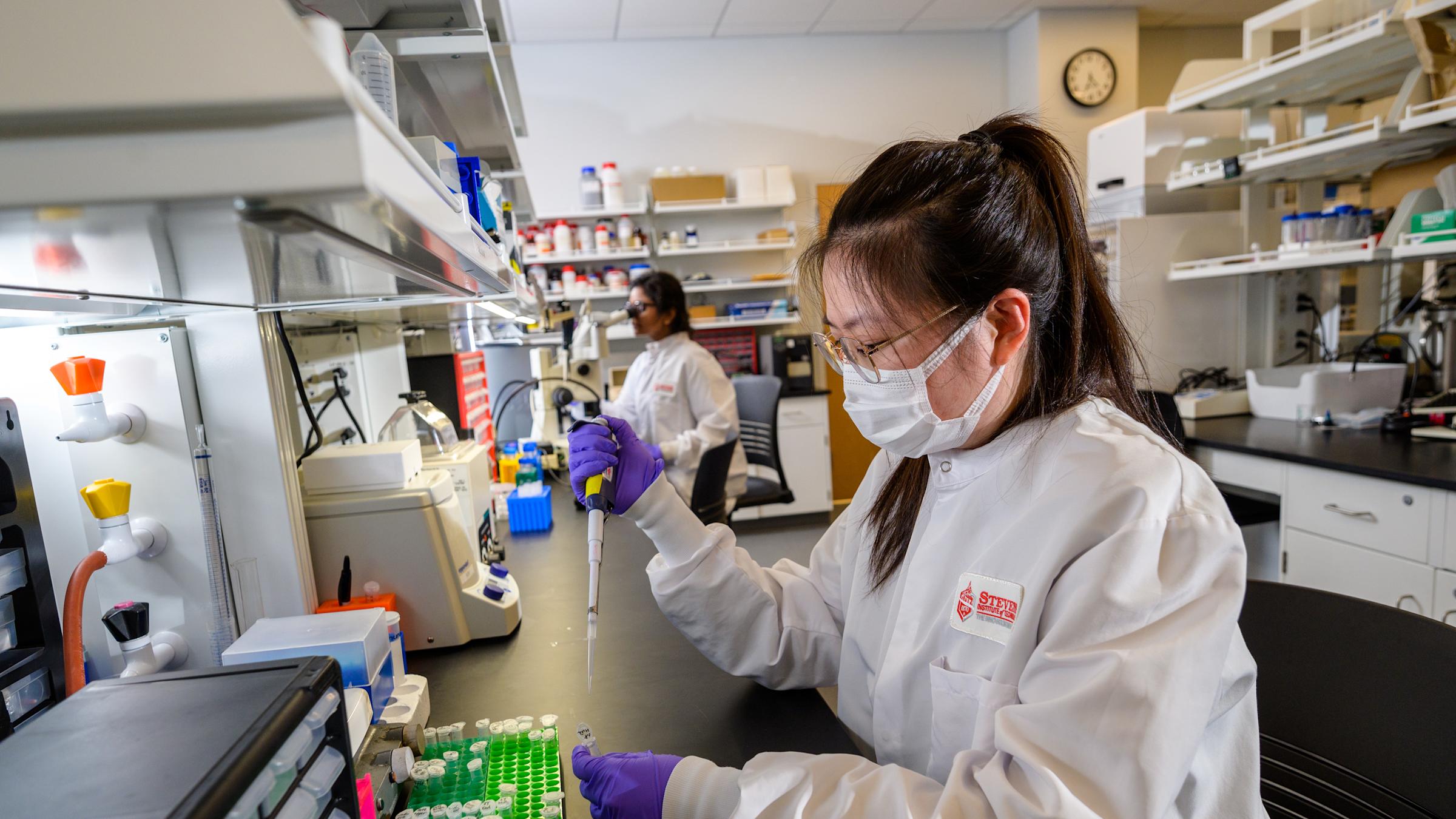 A female student in a mask holding a pipette working in the tissue engineering laboratory at the Center for Healthcare Innovation