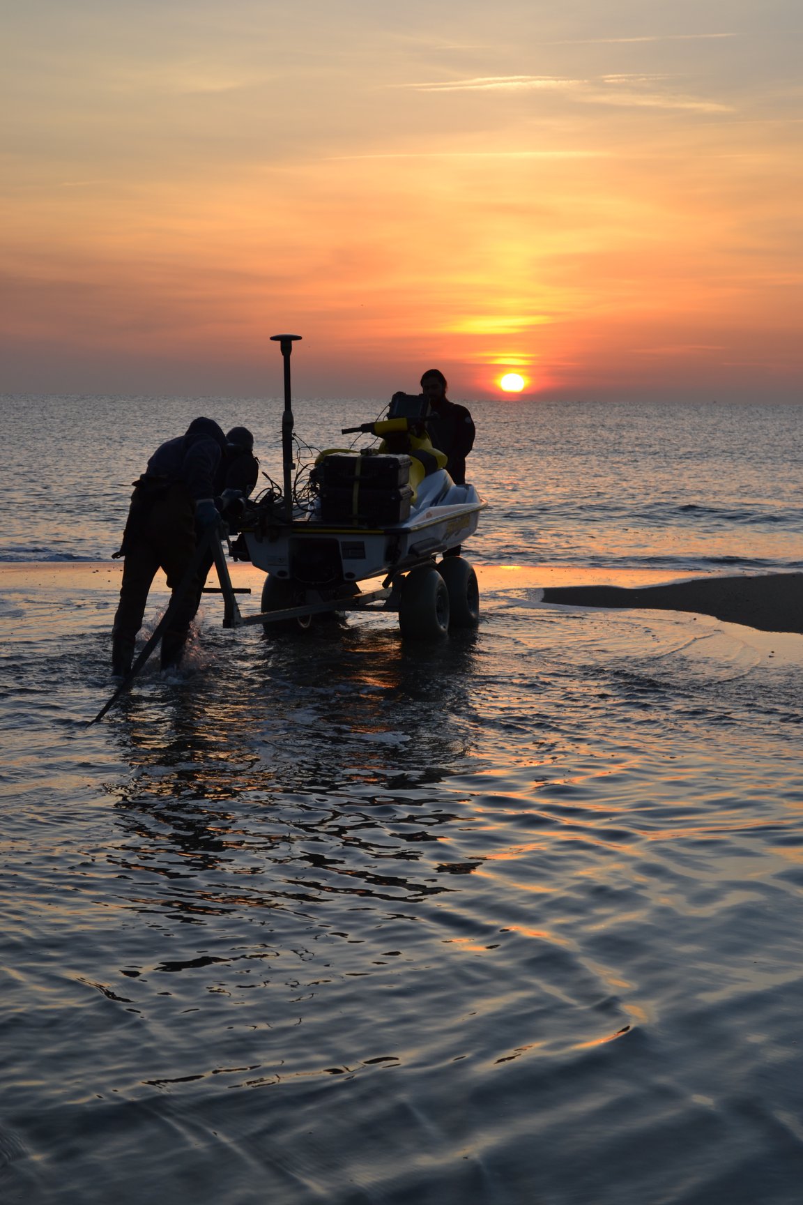 Members of the Department of Civil, Environmental and Ocean Engineering bring a device onto the shore with the sun going down.