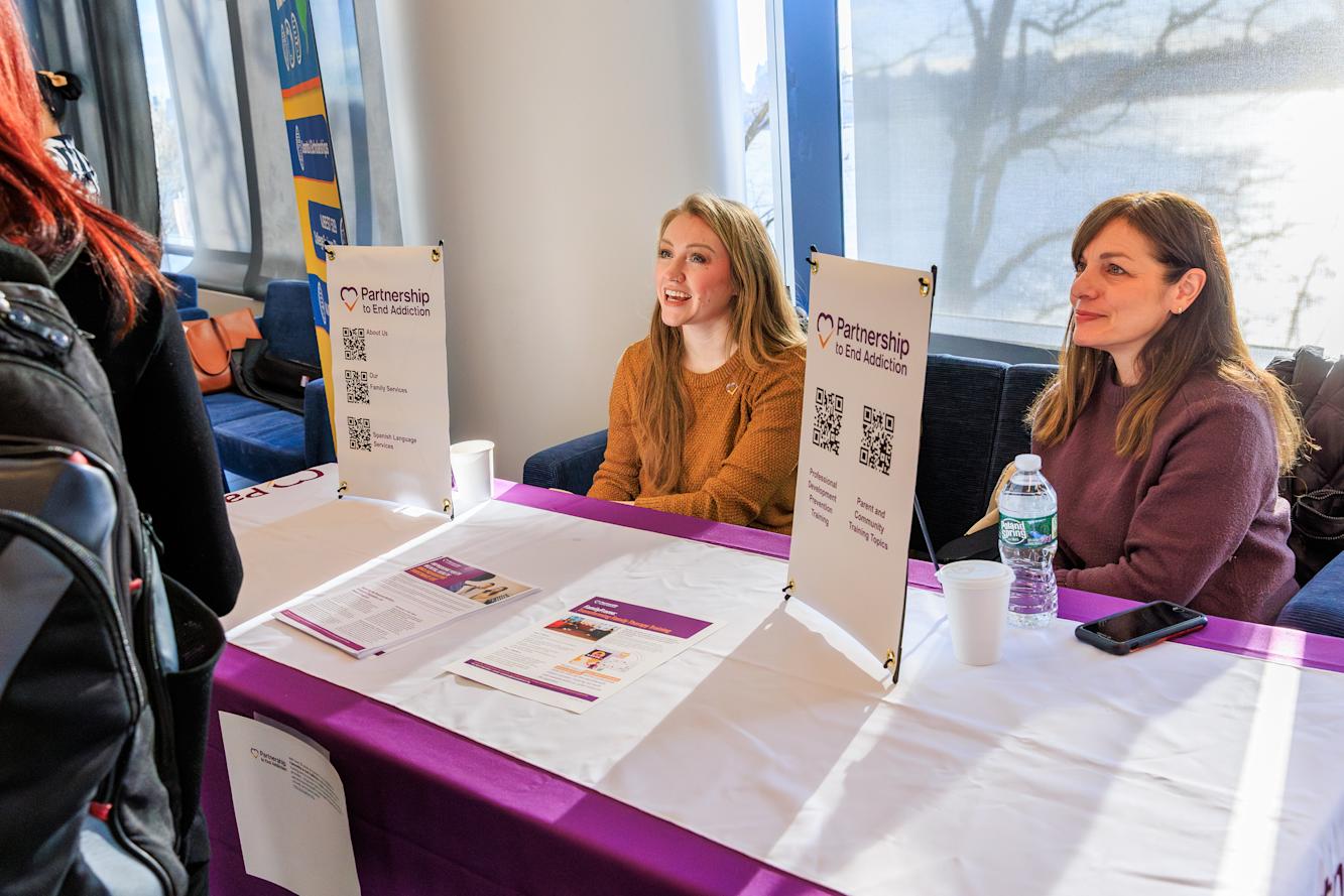 Two women sit at the Partnership to End Addiction table at the Resource Fair