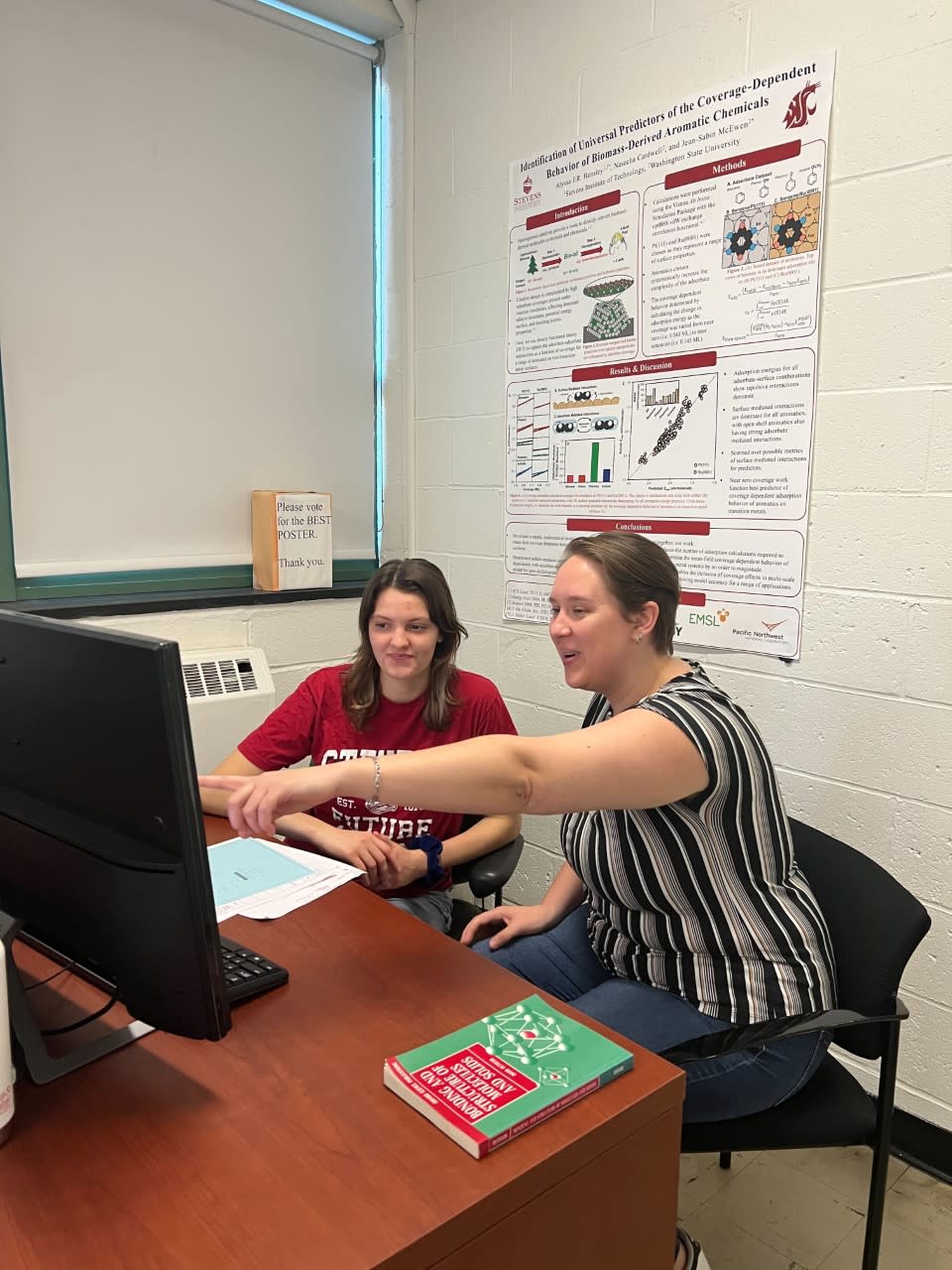 Photo of Furrick and Hensley pointing at a computer screen with a poster presentation on the wall behind them