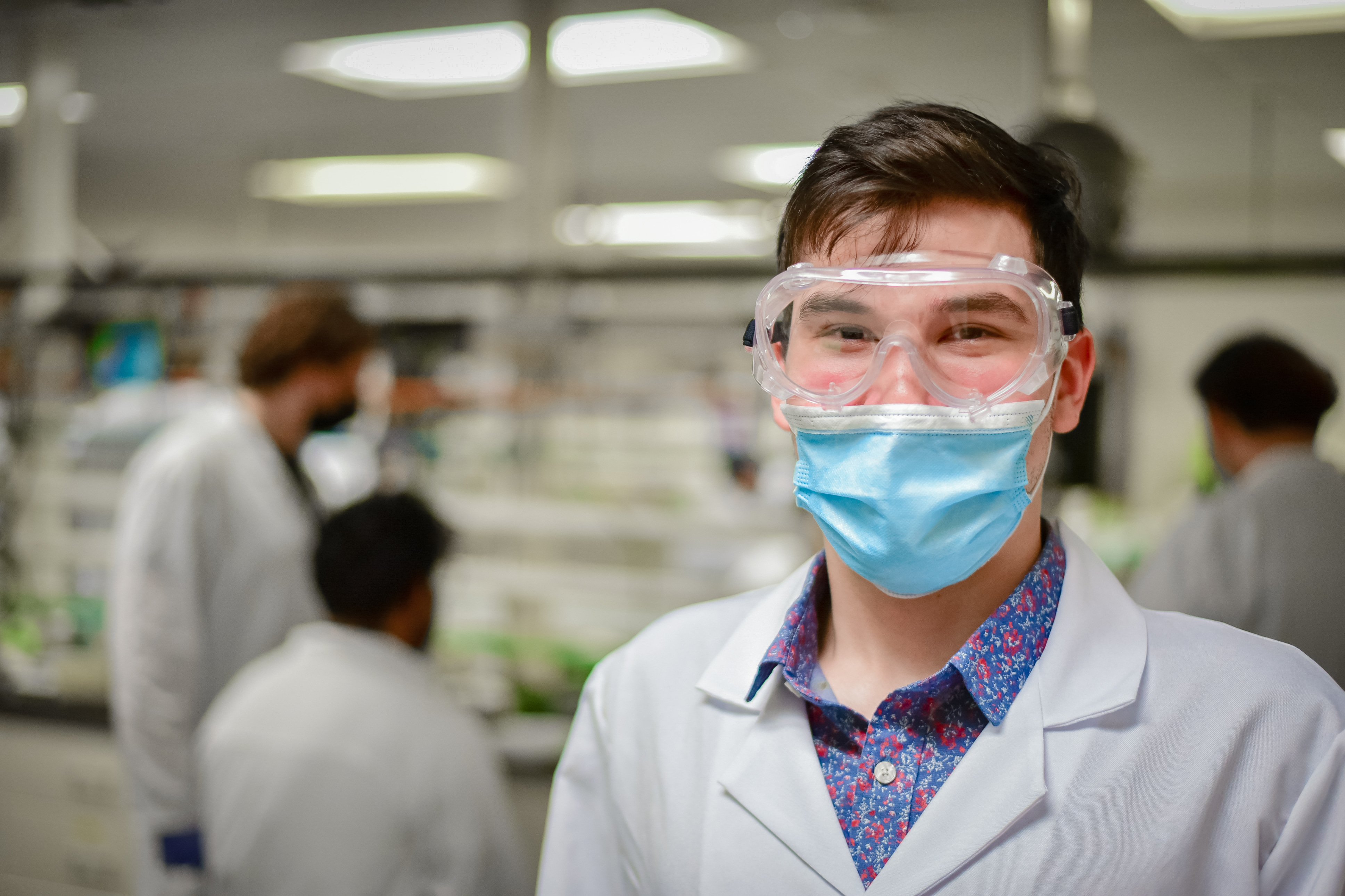 lab student with goggles and a mask on looking into camera