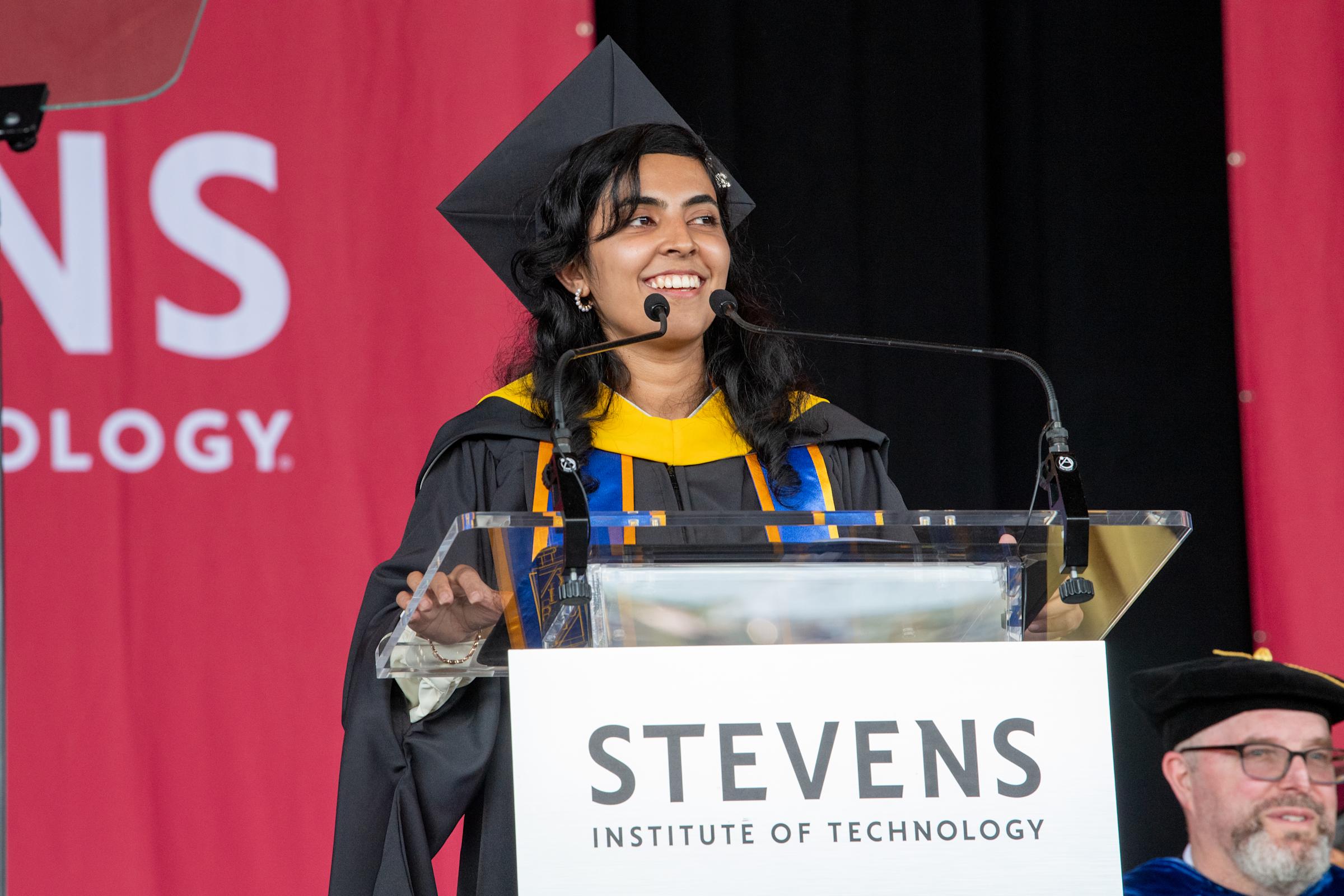 A woman in commencement regalia stands at a podium