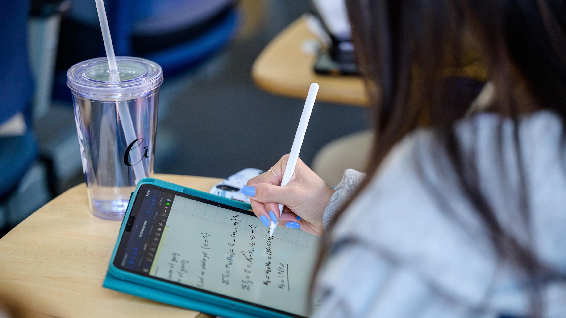 A student writes down formulas on a tablet in a classroom.