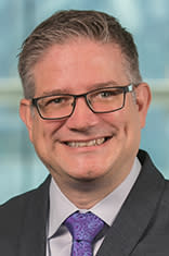 Headshot of Dr. Michael zur Muehlen in a dark suit with the New York City skyline in the background.