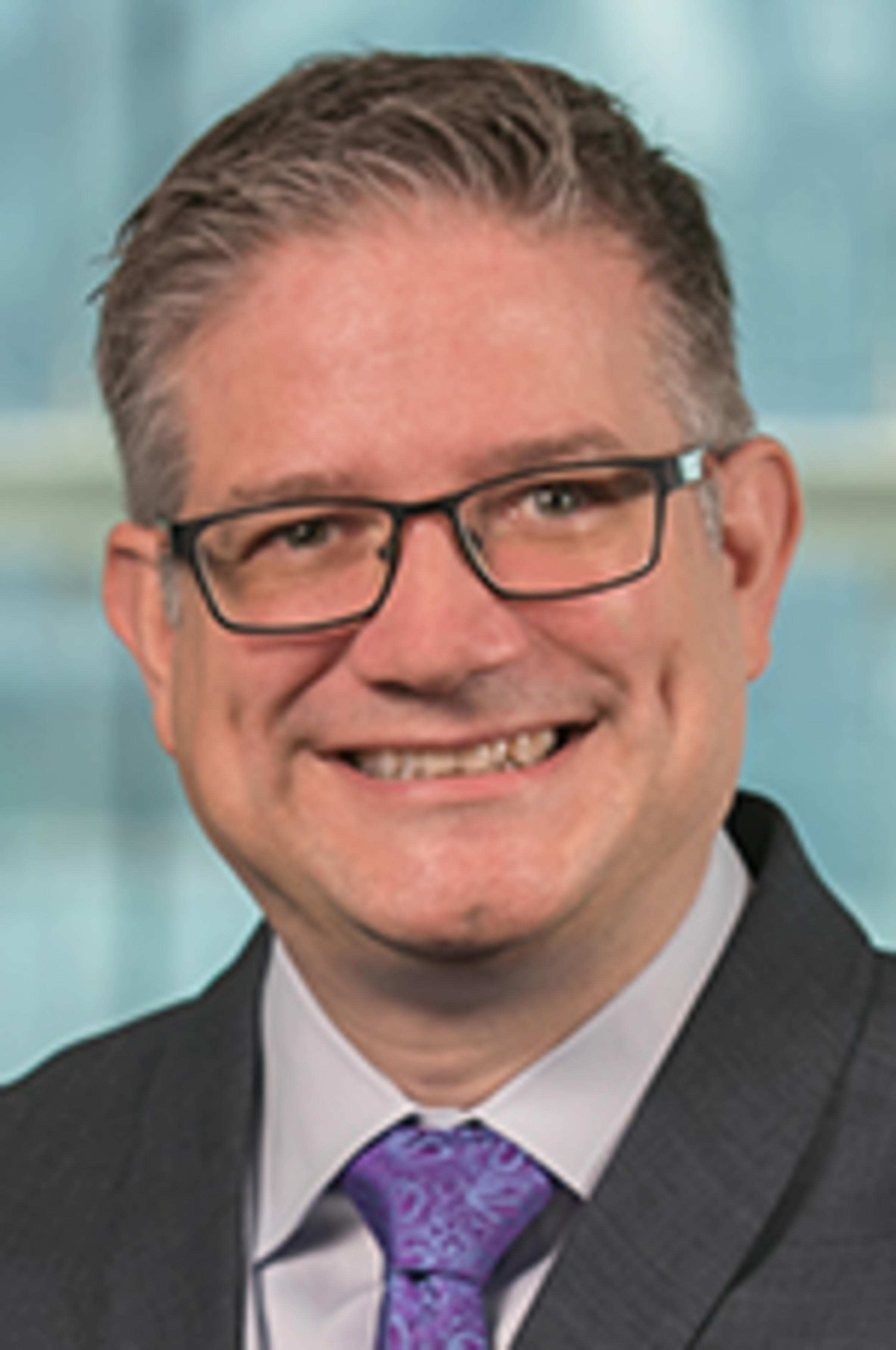 Headshot of Dr. Michael zur Muehlen in a dark suit with the New York City skyline in the background.