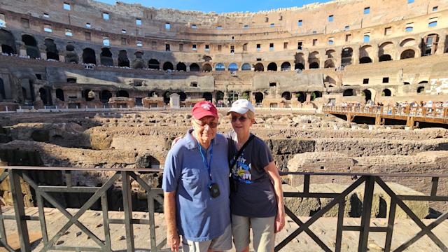 Barb and Jim Moraseski ’73 M.S. ’73 pose for picture together while in front of tourist destination of historical ruins, while Jim wears a Stevens baseball cap