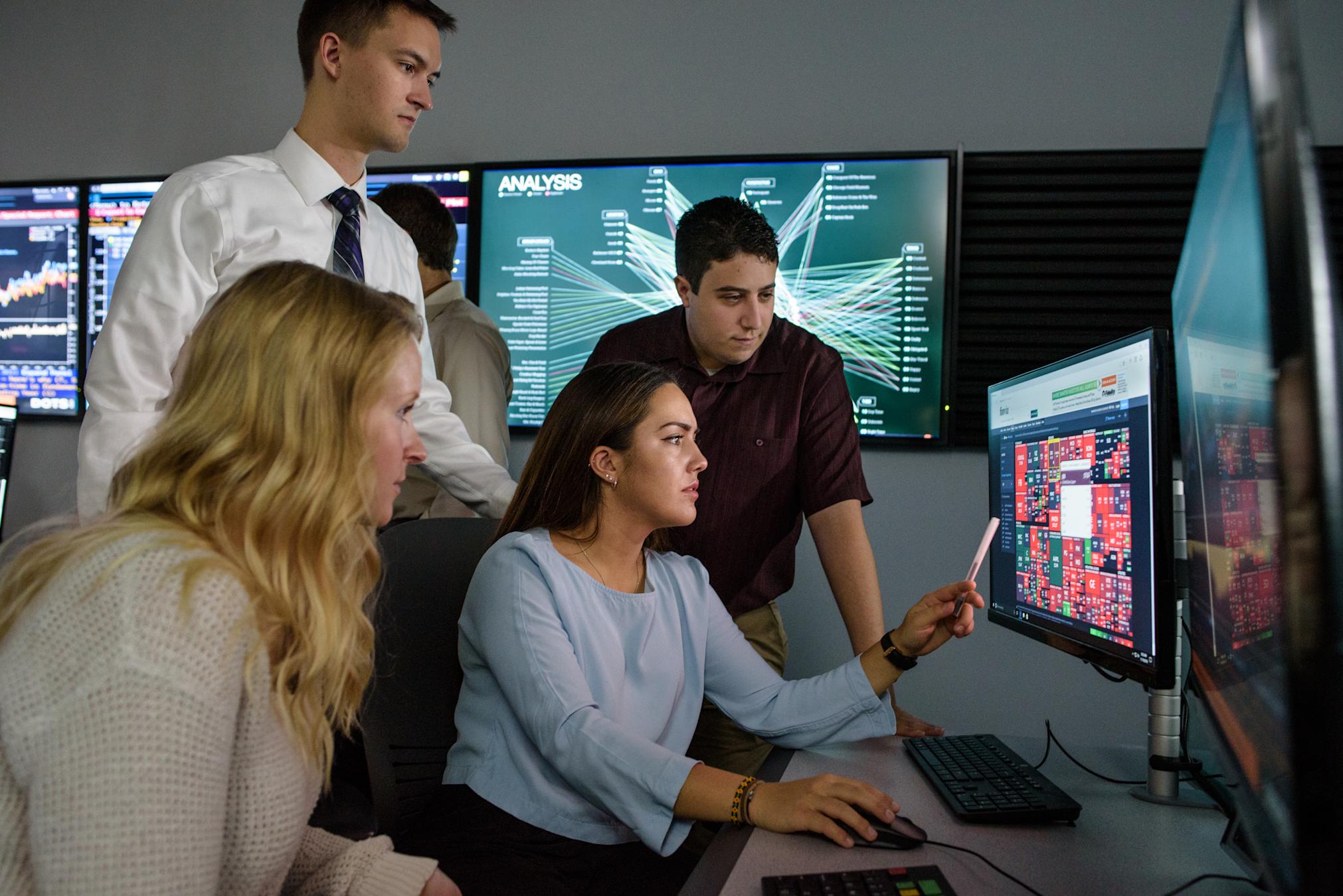 Student points to interesting information on computer monitor while other students look on, intrigued