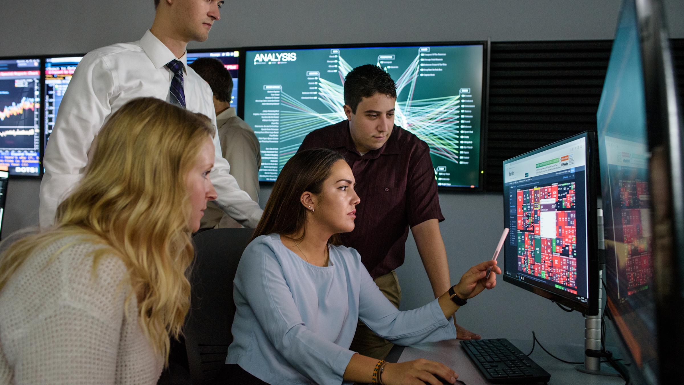 Student points to interesting information on computer monitor while other students look on, intrigued