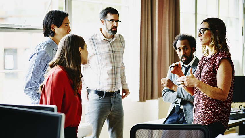 Five professionals hold an informal meeting in their office.
