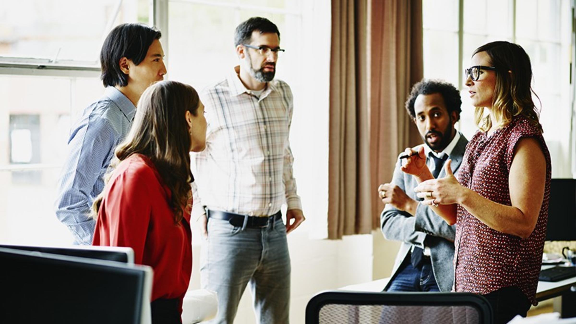 Five professionals hold an informal meeting in their office.