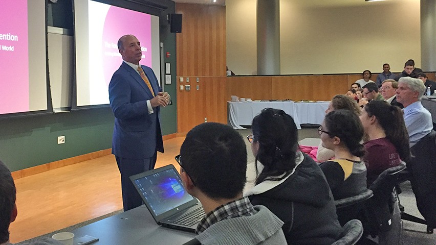 Frank Dramis, in a blue suit, speaking to a full auditorium on the Stevens campus in Hoboken.