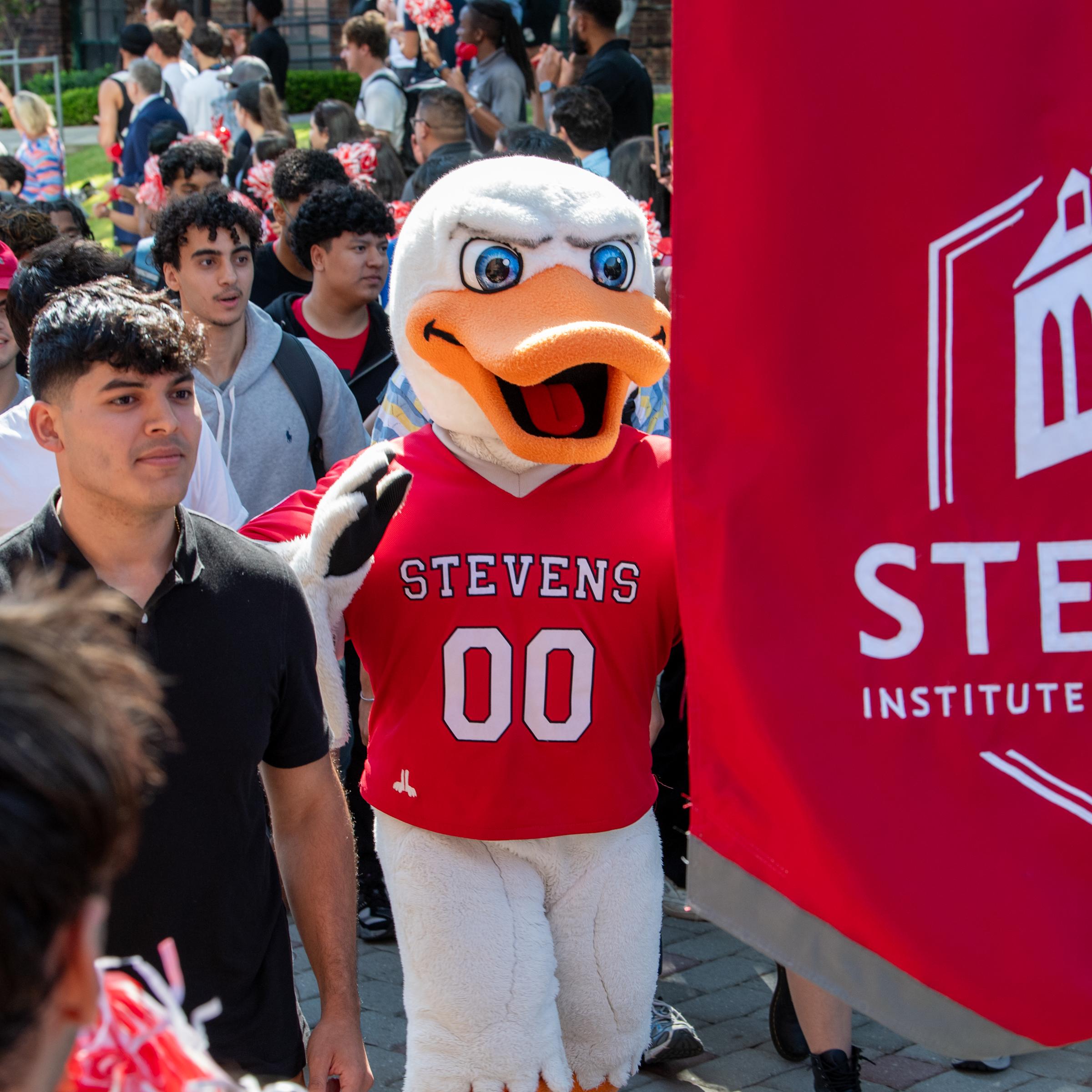 Students walk and cheer with duck mascot in springtime holding banner