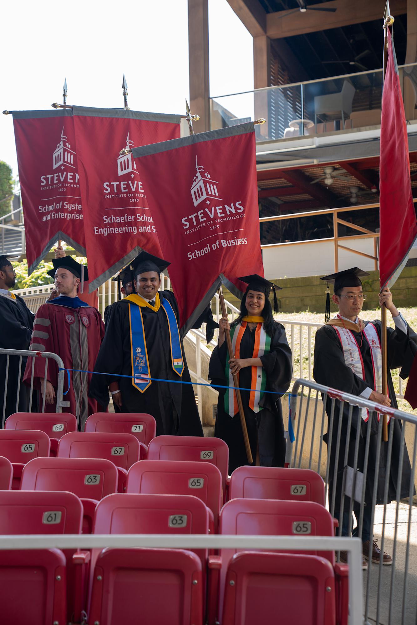 Two graduate students smile as they carry large School of Business banner for the graduate ceremony