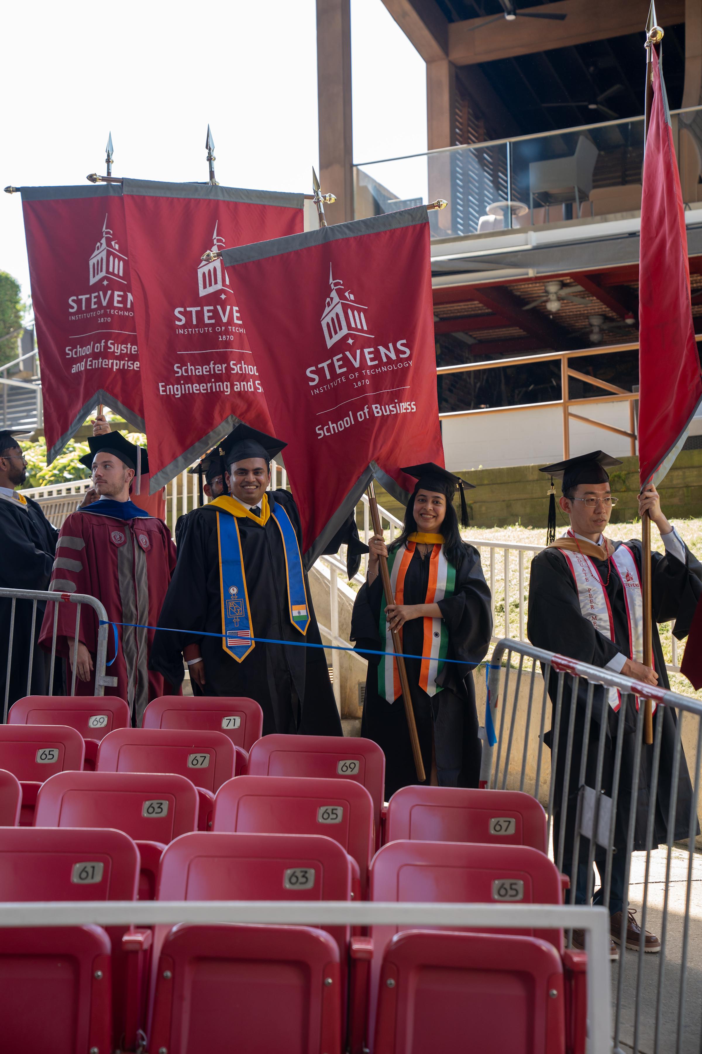 Two graduate students smile as they carry large School of Business banner for the graduate ceremony