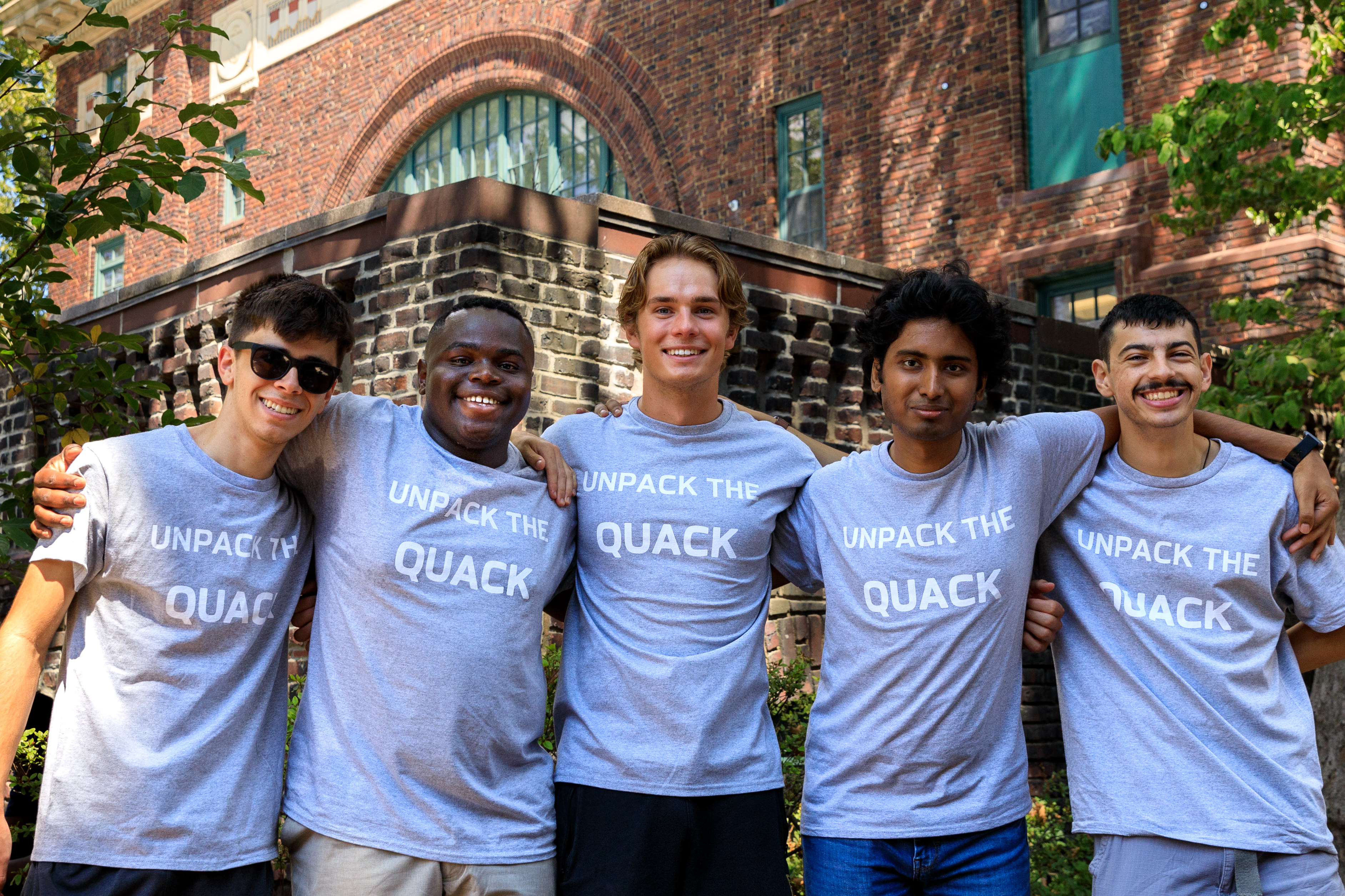 Five students stand with arms around each other wearing Unpack the Quack shirts