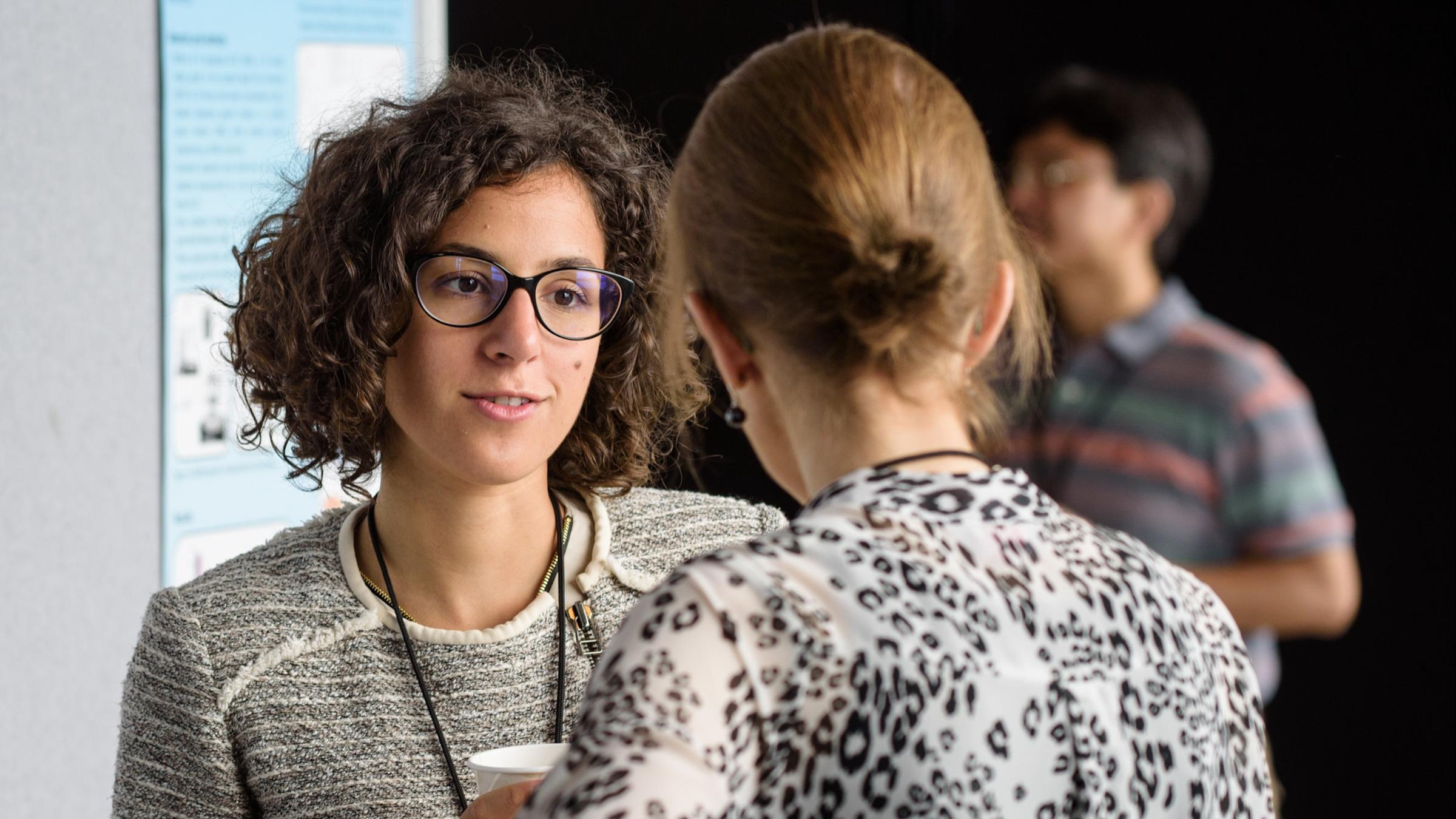 Female student at a poster session talking to a female professor.
