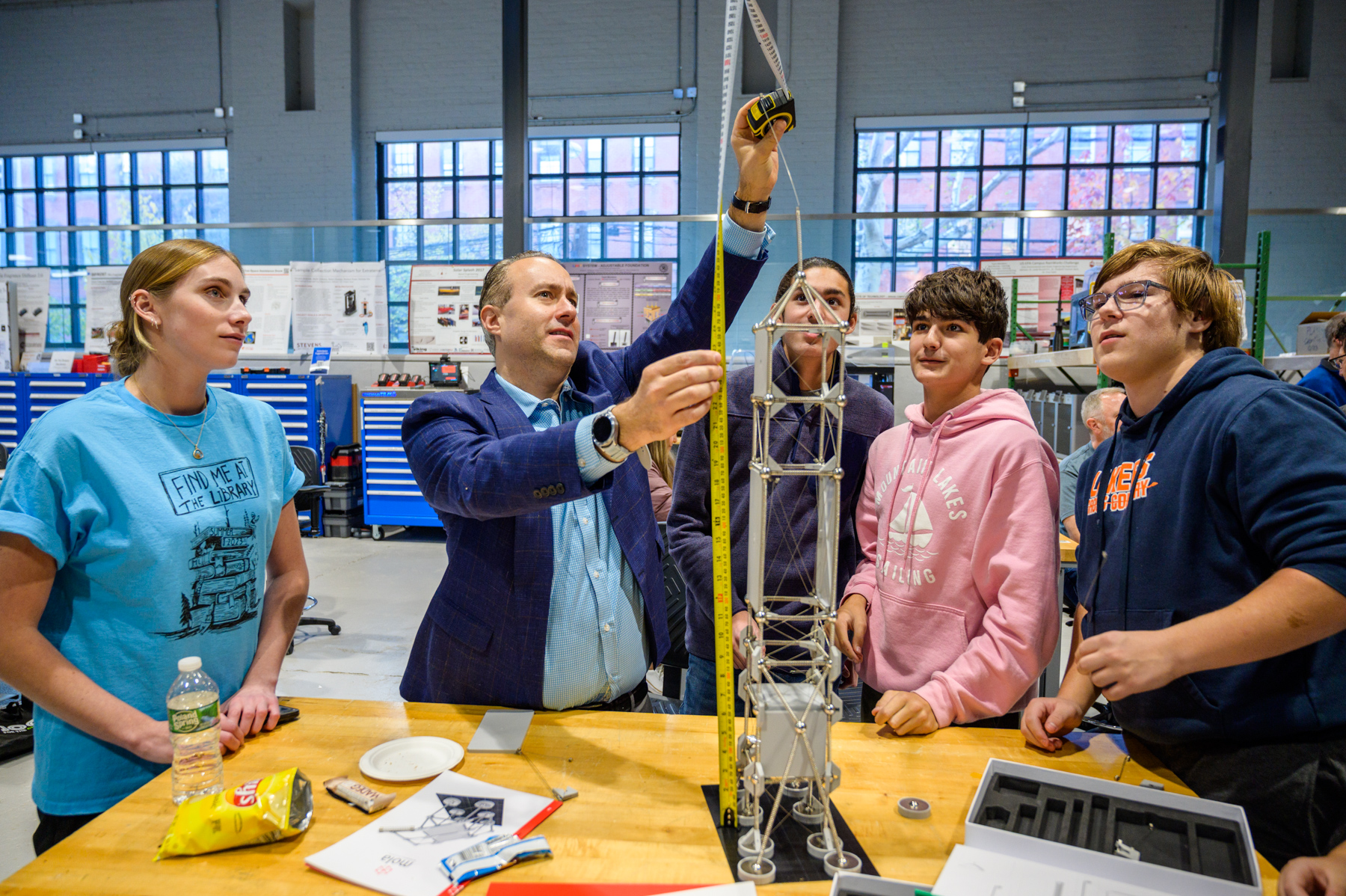 Photo of a man holding up a measuring tape to a tower while four students surround him looking up