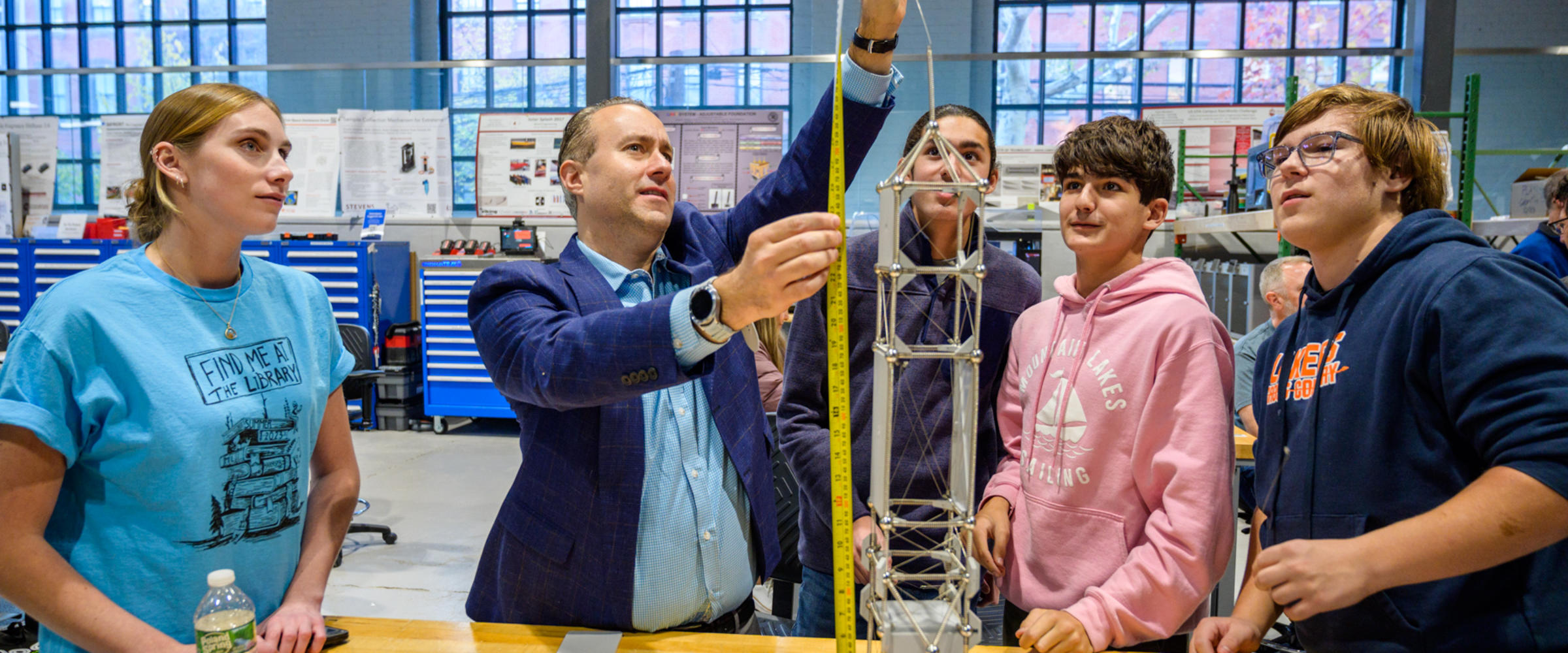 Photo of a man holding up a measuring tape to a tower while four students surround him looking up