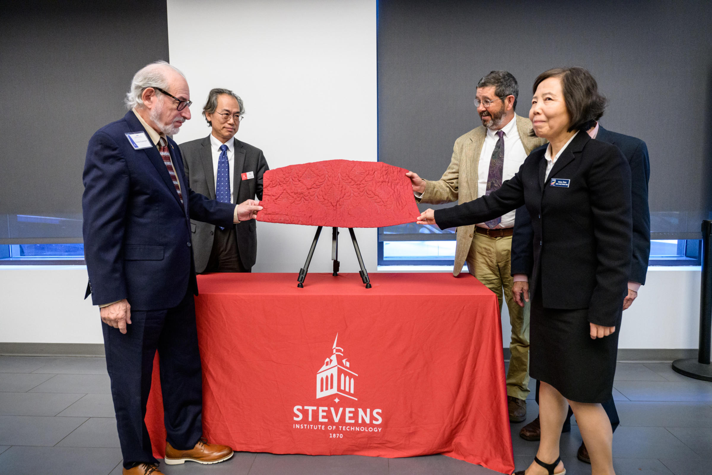 Four people prepare to uncover a plaque from behind a red covering.