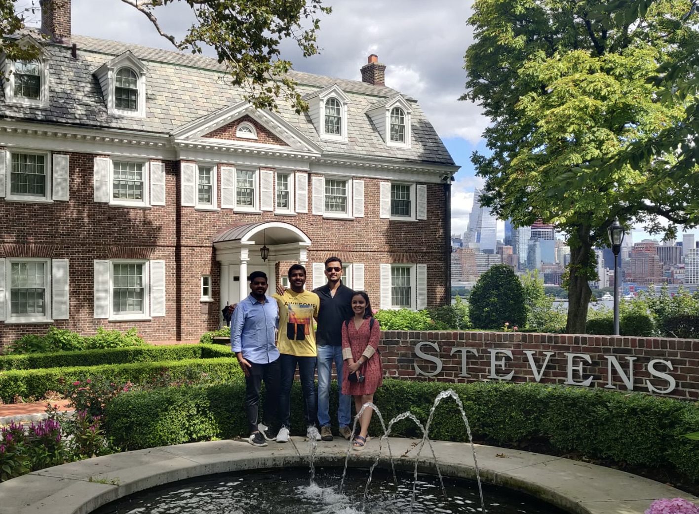 Rhythm Goyal stands with her family in front of the fountain on the Stevens campus with the New York City skyline visible in the background.
