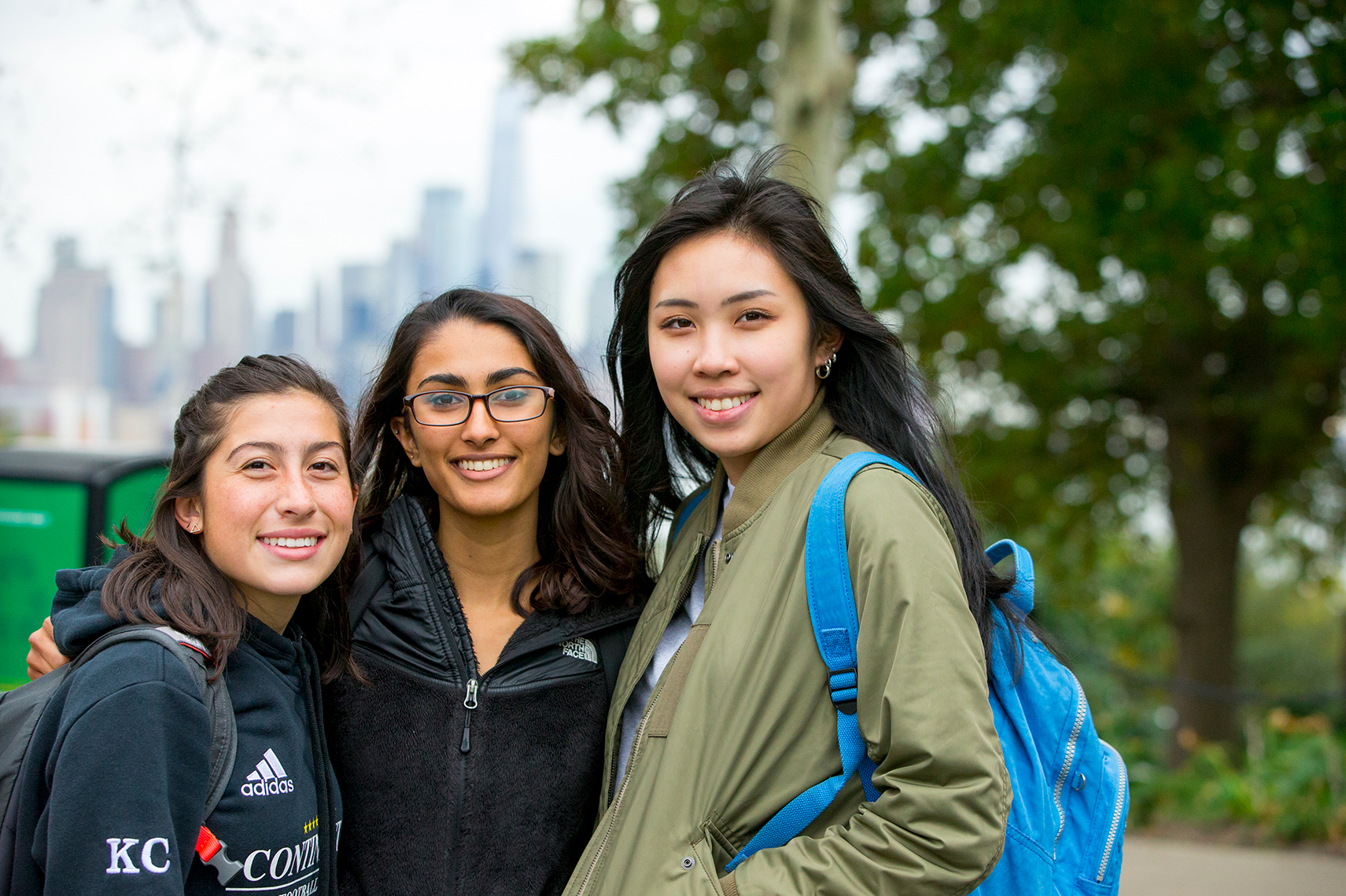 3 female students smiling with NYC skyline background
