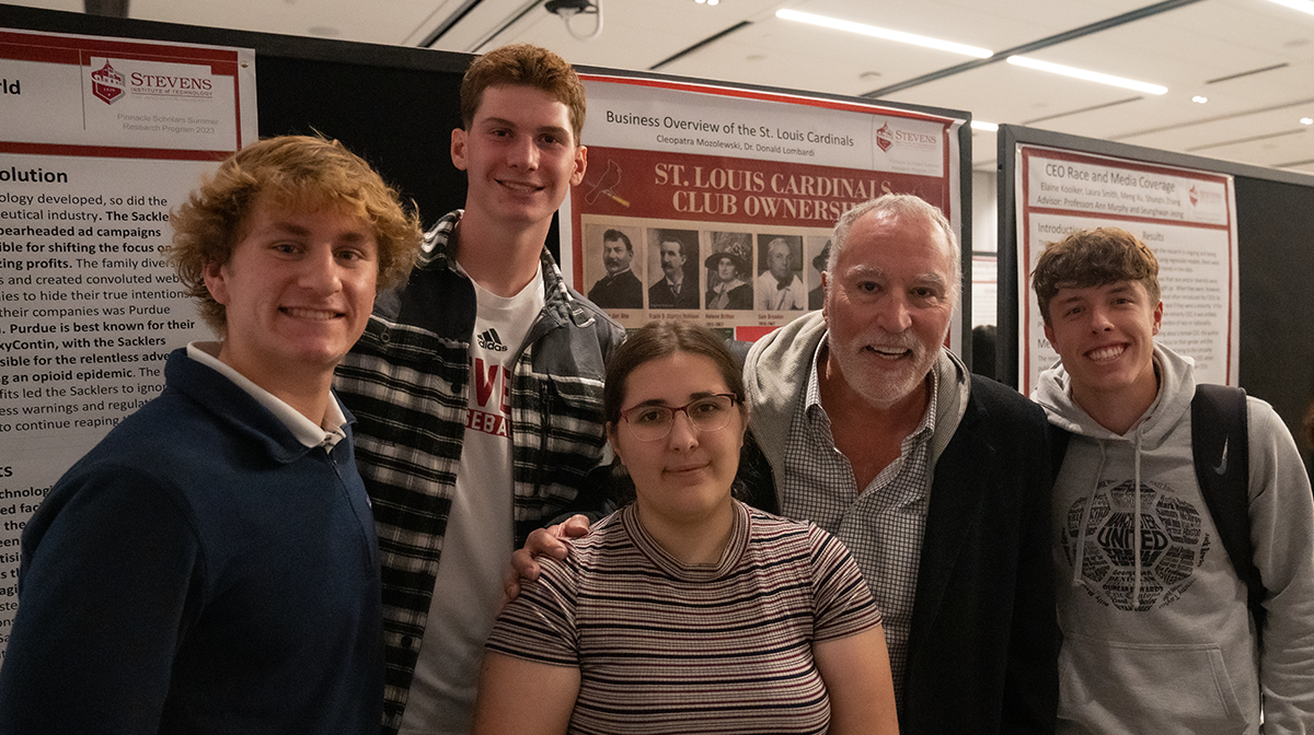 Professor Don Lombardi stands with a group of students at the 2023 Pinnacle Scholars poster exhibition.
