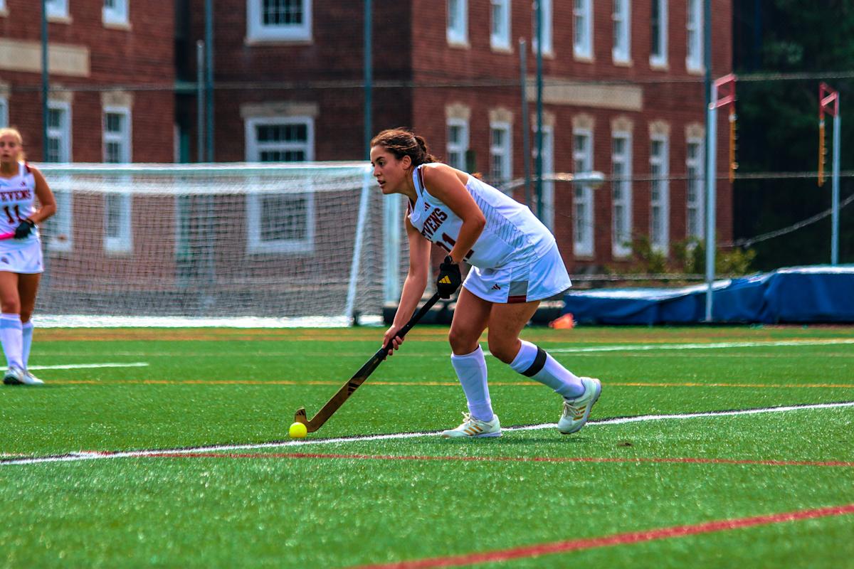 Emilia runs on the field with the ball while playing field hockey